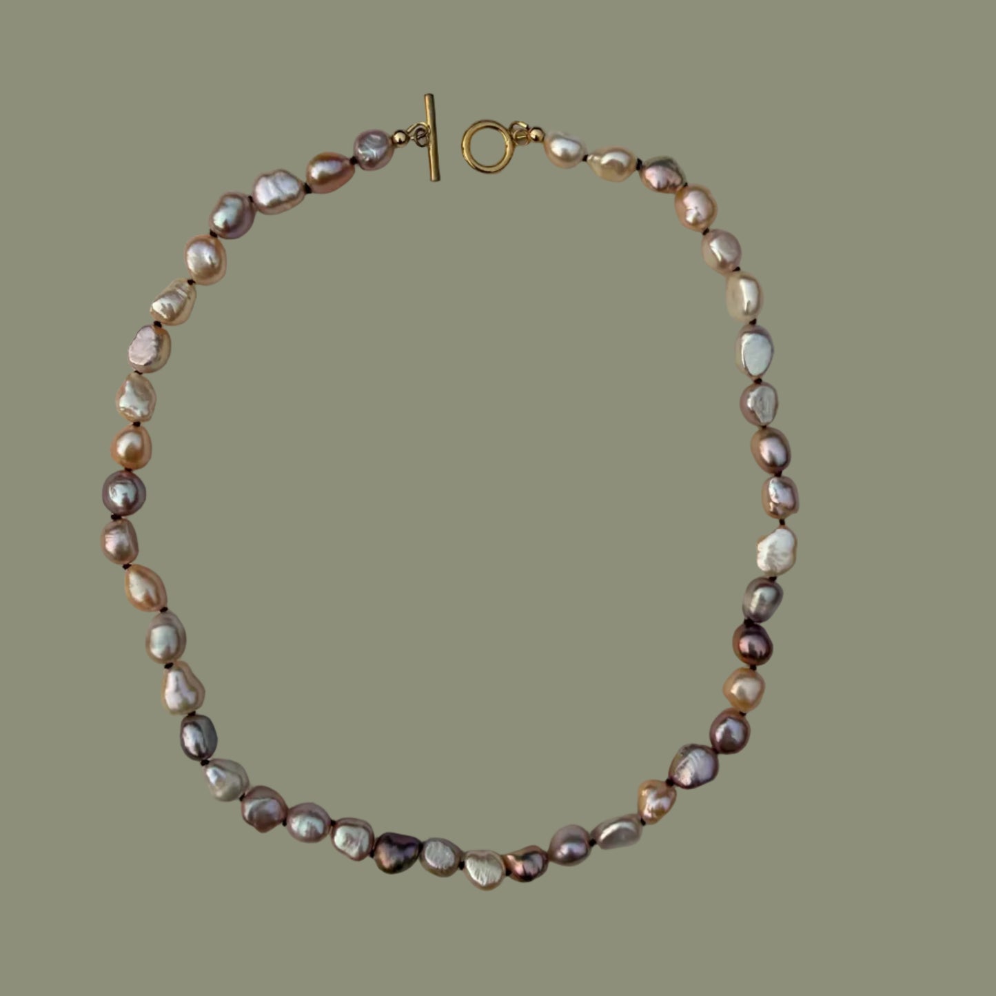 A baroque pearl necklace with a gold toggle clasp, displayed on a solid olive green background.