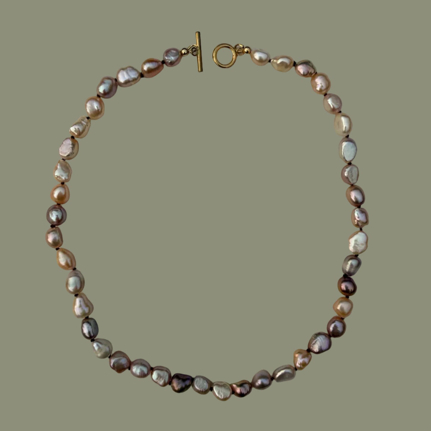 A baroque pearl necklace with a gold clasp, displayed on a solid olive green background.