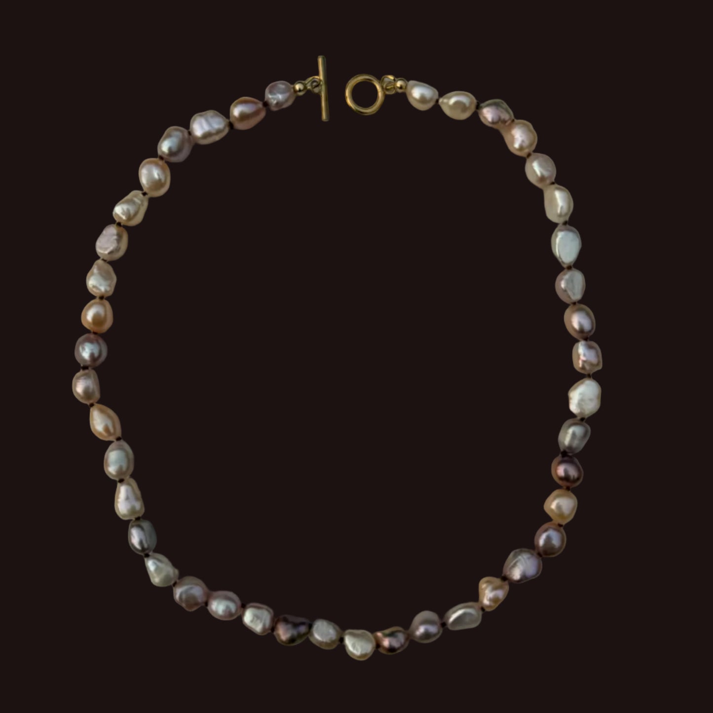 A strand necklace made of irregular baroque pearls in muted gray, taupe, and cream tones, with a gold-tone toggle clasp, shown on a solid dark brown background.