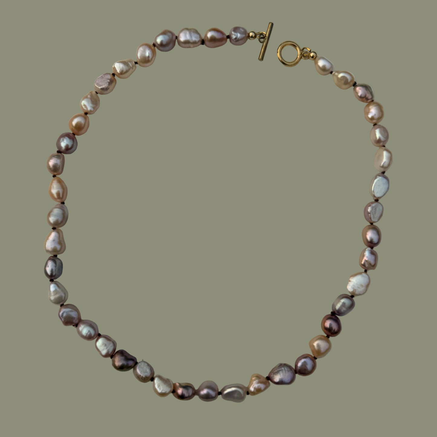 A baroque pearl necklace with iridescent pink, purple, and white pearls, accented by a gold toggle clasp, displayed on a neutral light gray background.