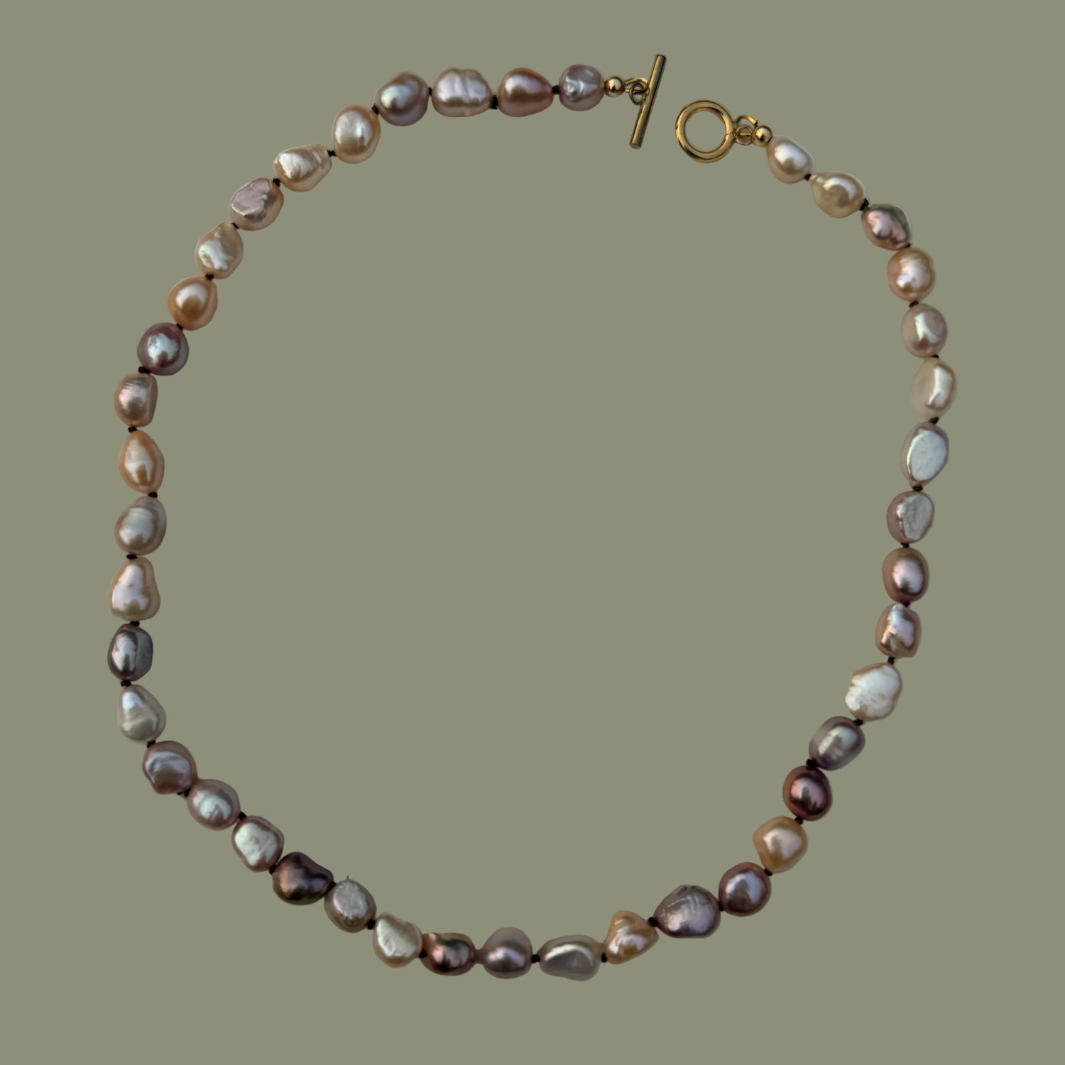 A baroque pearl necklace with iridescent pink, purple, and white pearls, accented by a gold toggle clasp, displayed on a neutral light gray background.