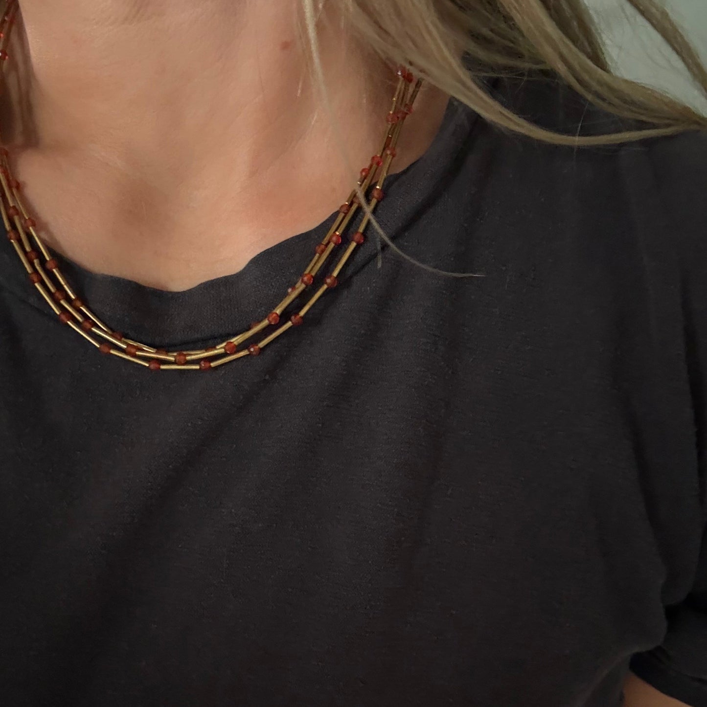 Close-up of a person wearing a multi-strand beaded necklace with red and gold beads over a black t-shirt.