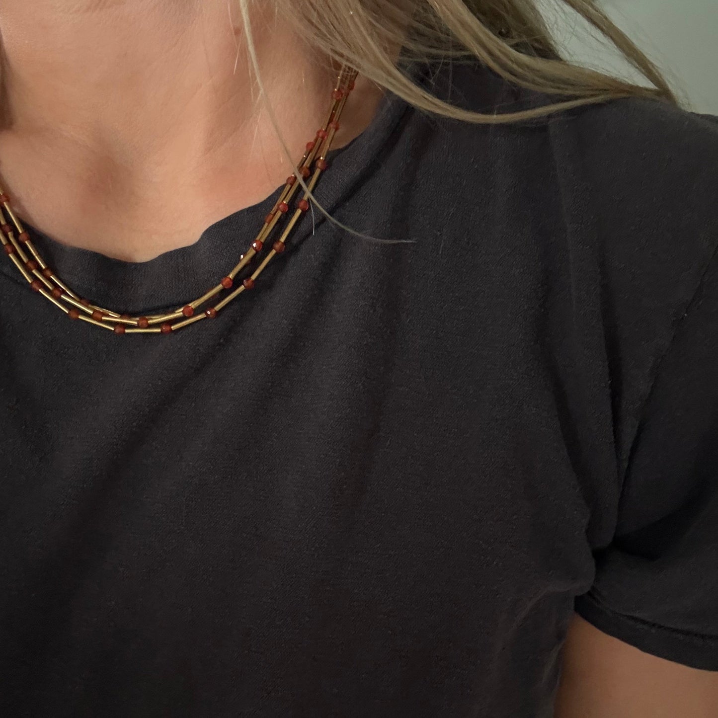 Close-up of a person wearing a black short-sleeve crewneck t-shirt and a multi-strand beaded necklace with red, orange, and gold beads.