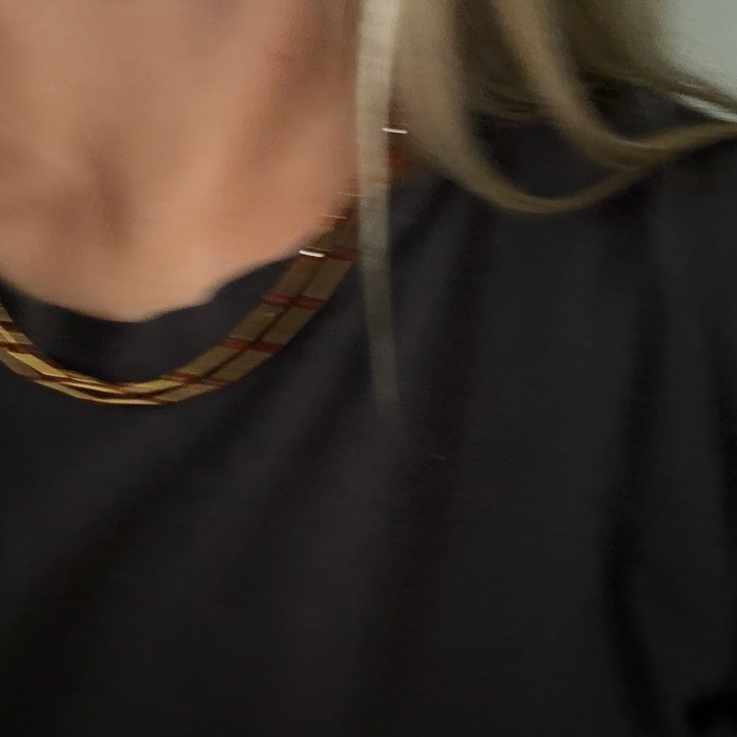 A close-up shot of a person wearing a thick braided gold and red plaid necklace over a black t-shirt.