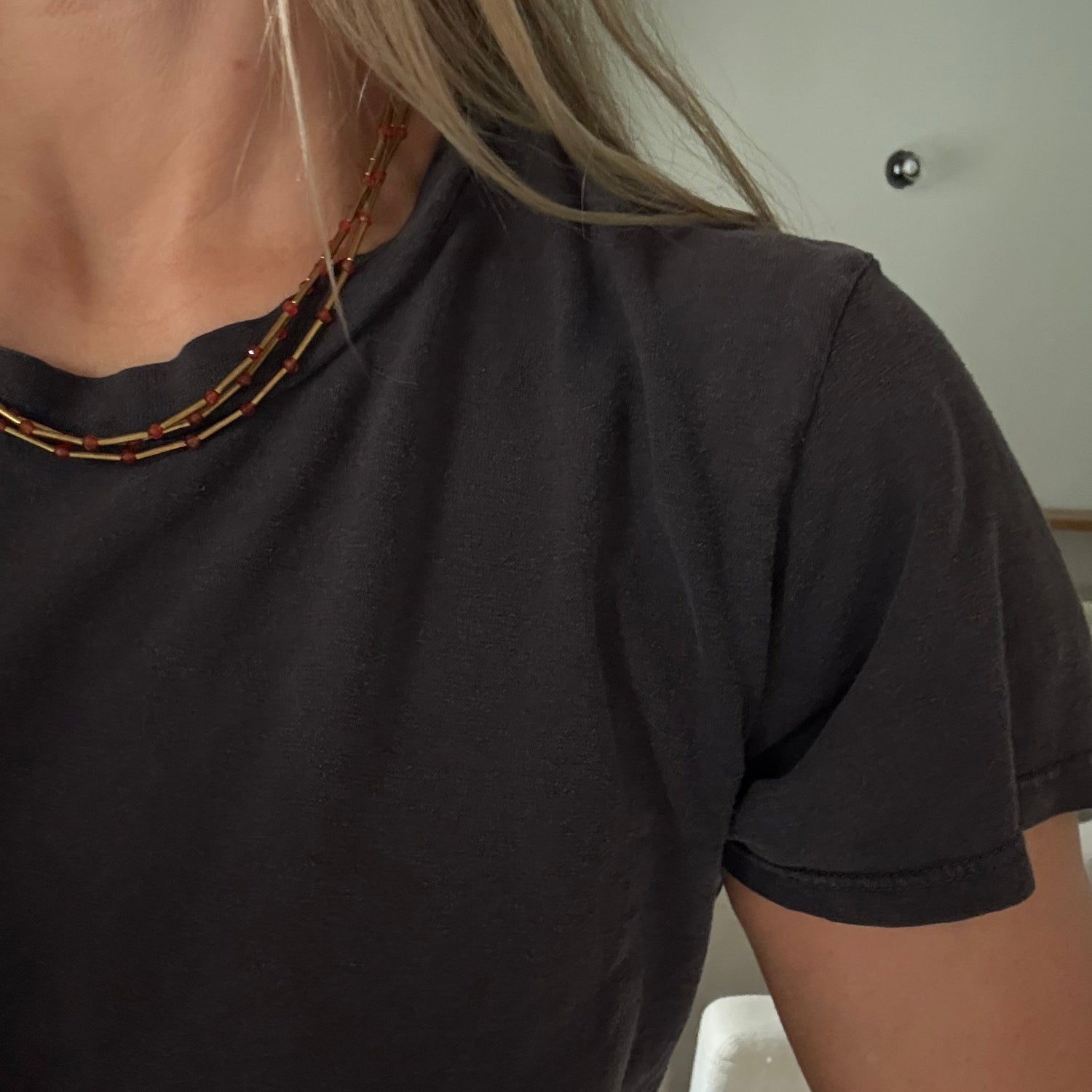 A close-up of a person wearing a dark charcoal gray short-sleeve t-shirt and a multi-strand beaded necklace.
