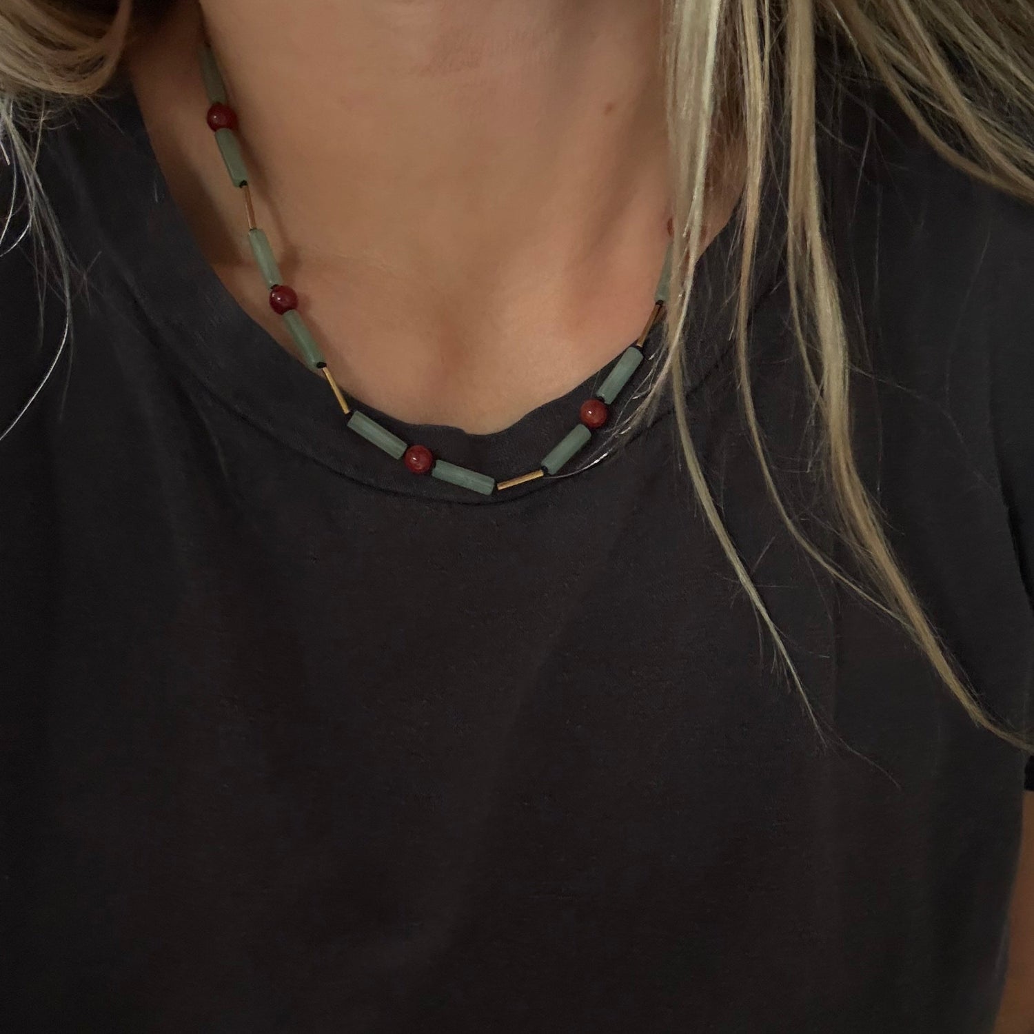 A close-up of a person wearing a beaded necklace with light blue-green beads and small red beads, paired with a black t-shirt.
