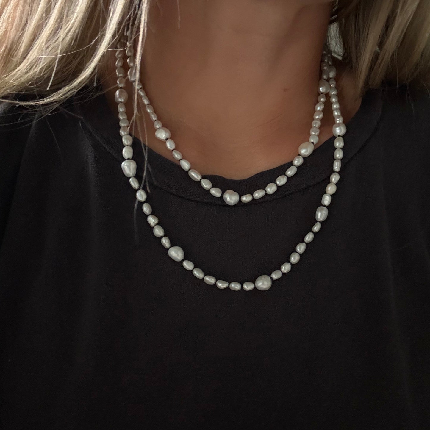 A close-up of a person wearing a double-strand pearl necklace with irregular baroque-style pearls over a black top.