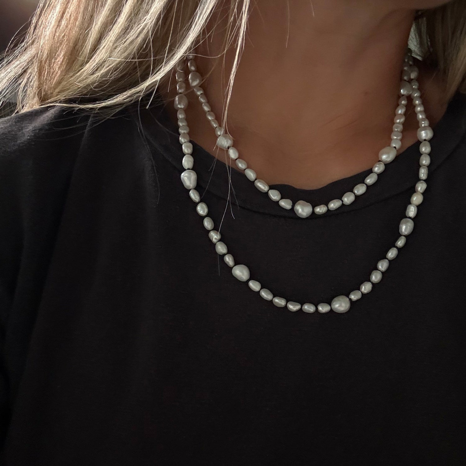 A close-up of a person wearing a double-strand pearl necklace with irregular white beads over a black top.