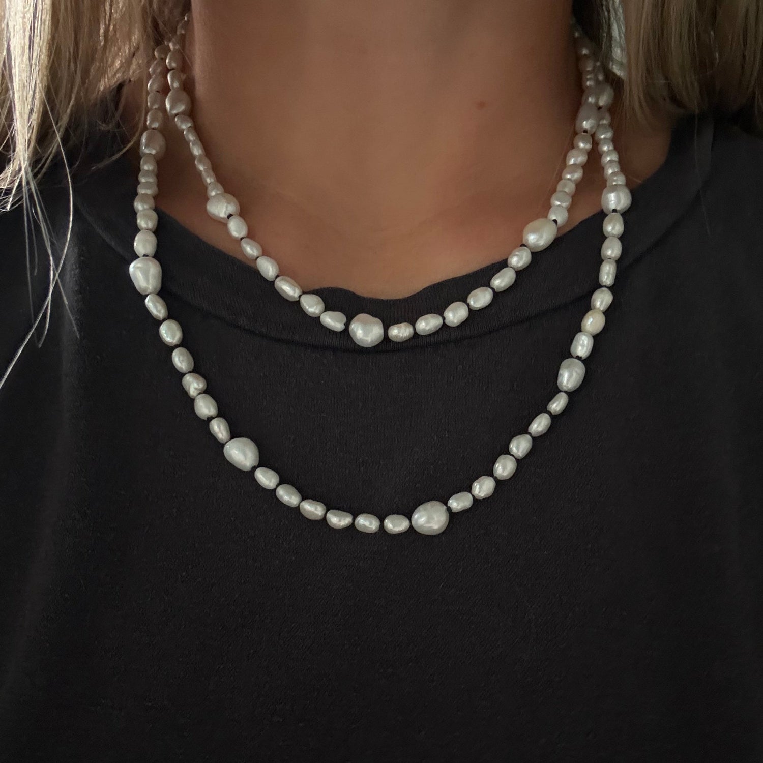 A close-up of a person wearing a double-strand pearl necklace with irregular baroque-style beads over a black top.