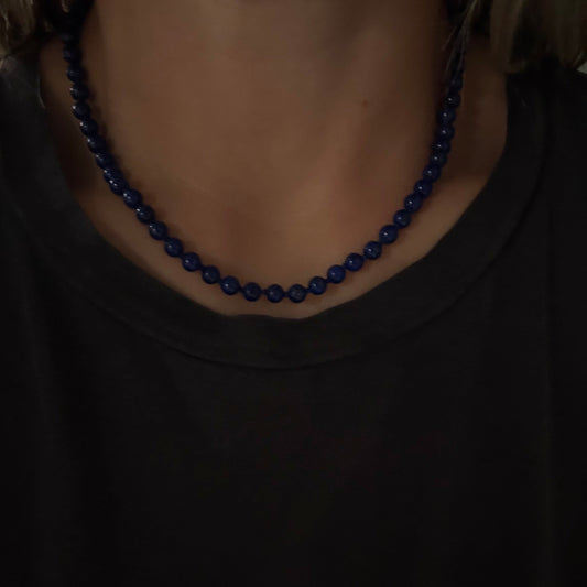 A close-up of a person wearing a dark blue beaded necklace with a black t-shirt.