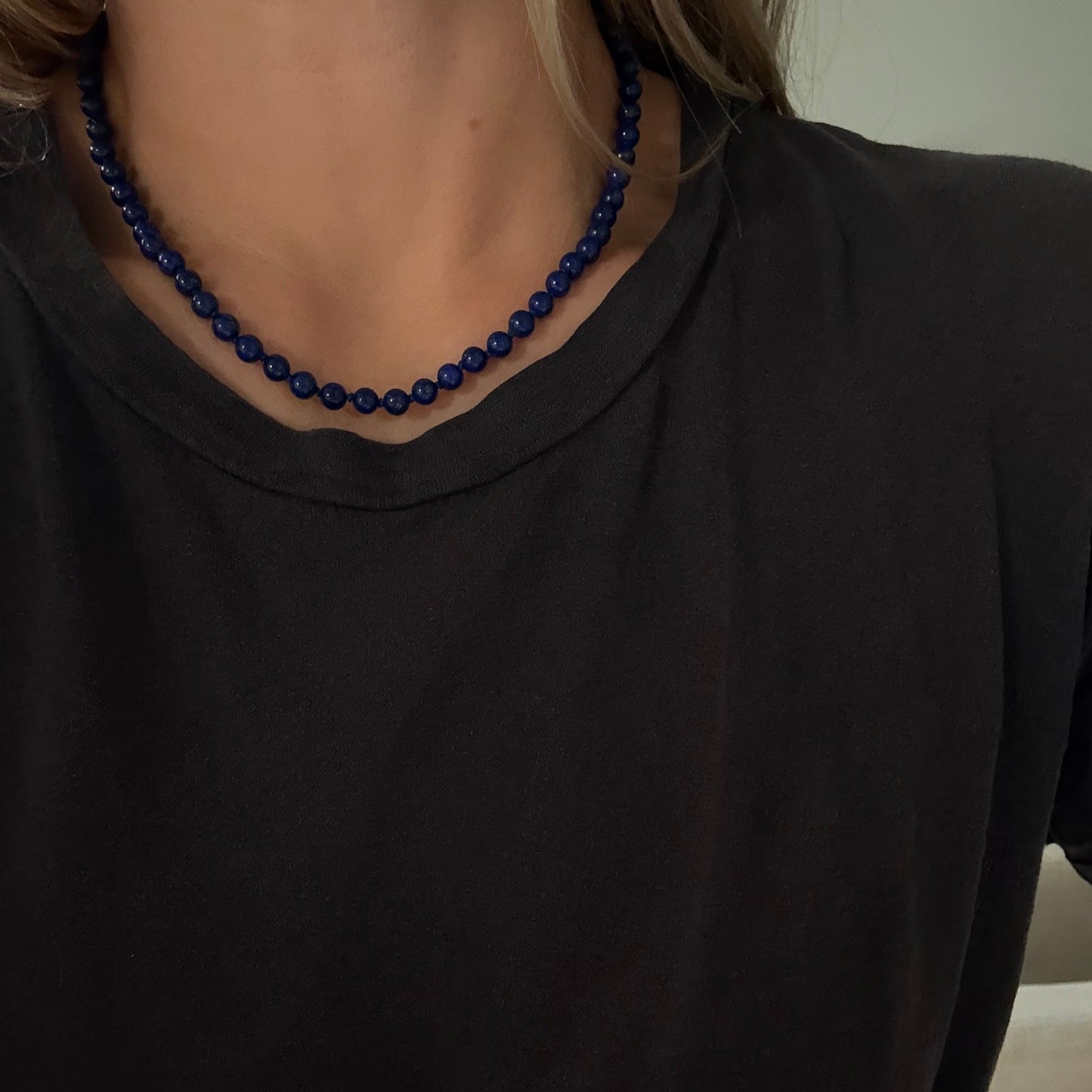A close-up of a person wearing a dark navy blue beaded necklace with a black t-shirt.