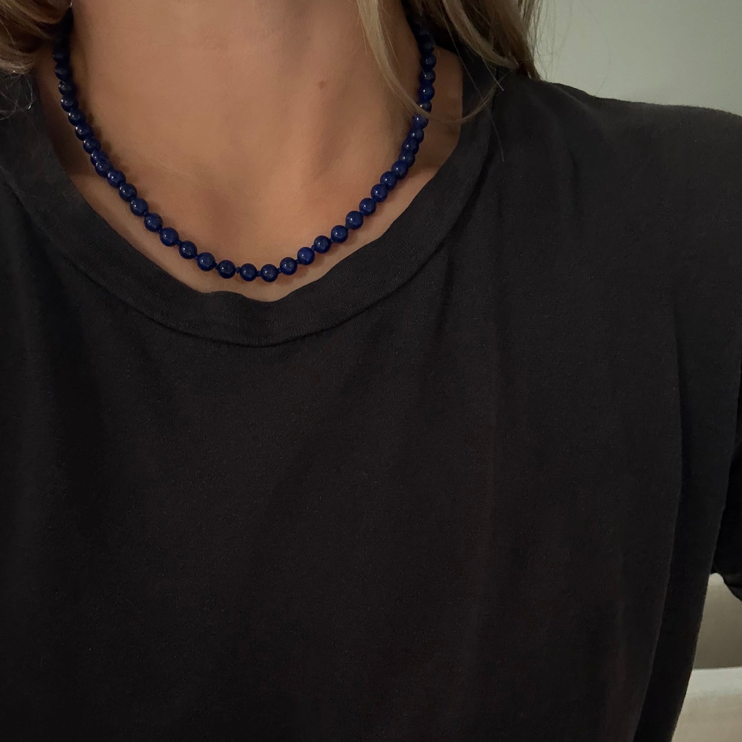 A close-up of a person wearing a dark navy blue beaded necklace with a black t-shirt.