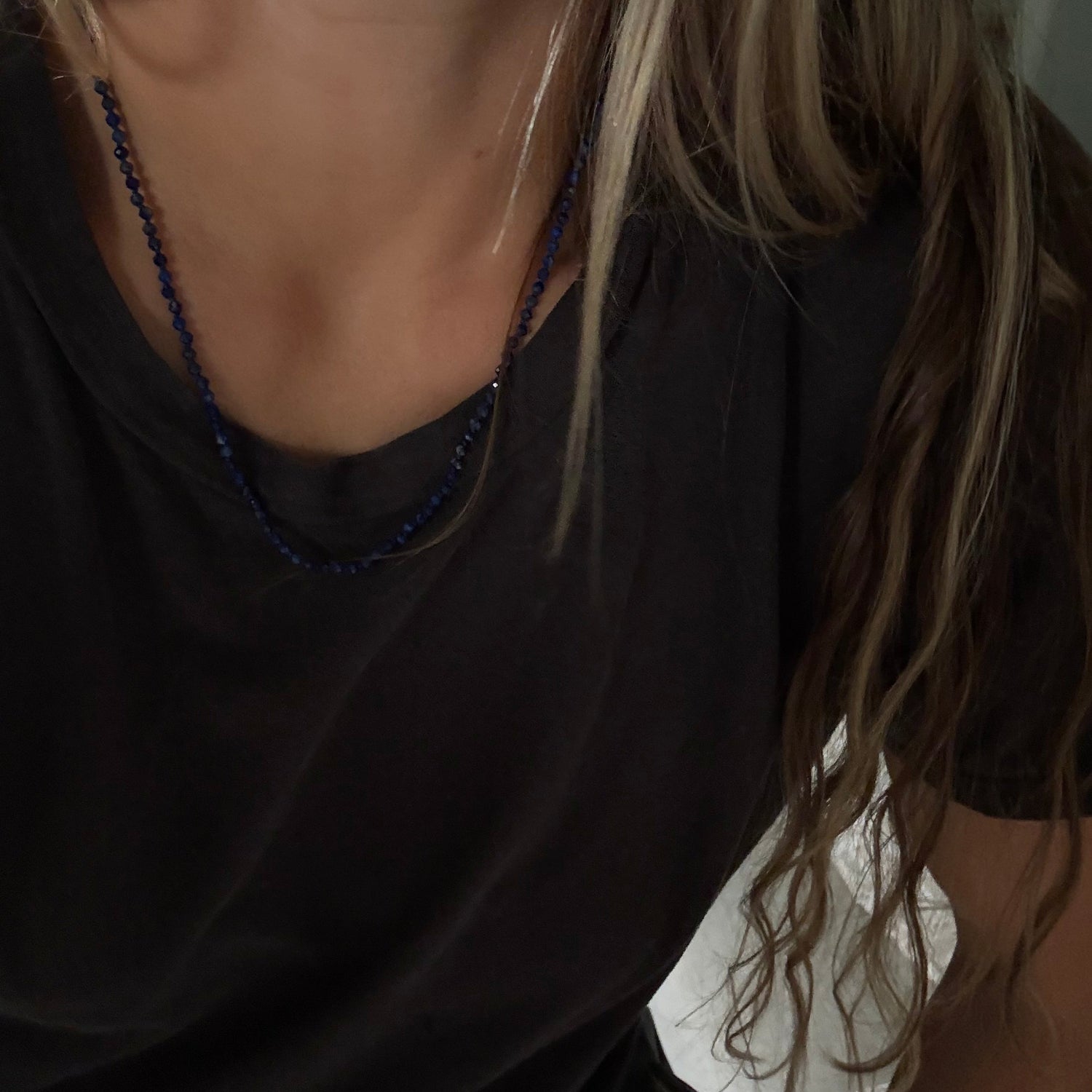 A close-up lifestyle shot of a person wearing a dark navy blue beaded necklace with a black t-shirt.