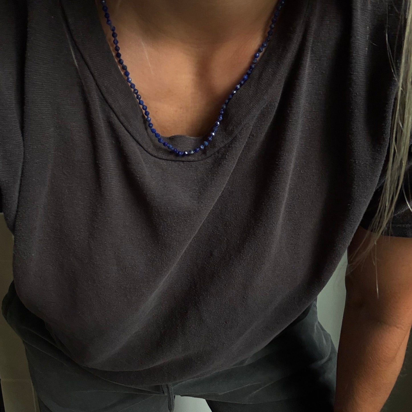 A close-up of a person wearing a dark charcoal gray t-shirt and matching pants, accessorized with a blue beaded necklace.
