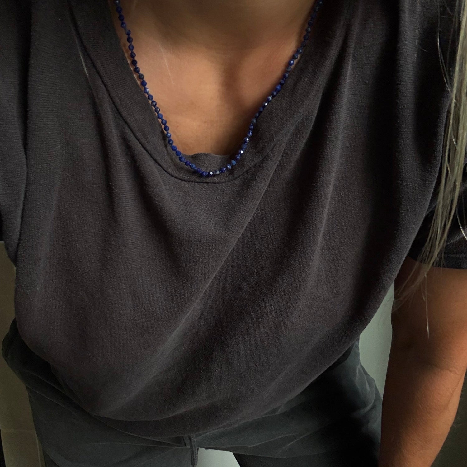 A close-up of a person wearing a dark charcoal gray t-shirt and matching pants, accessorized with a blue beaded necklace.