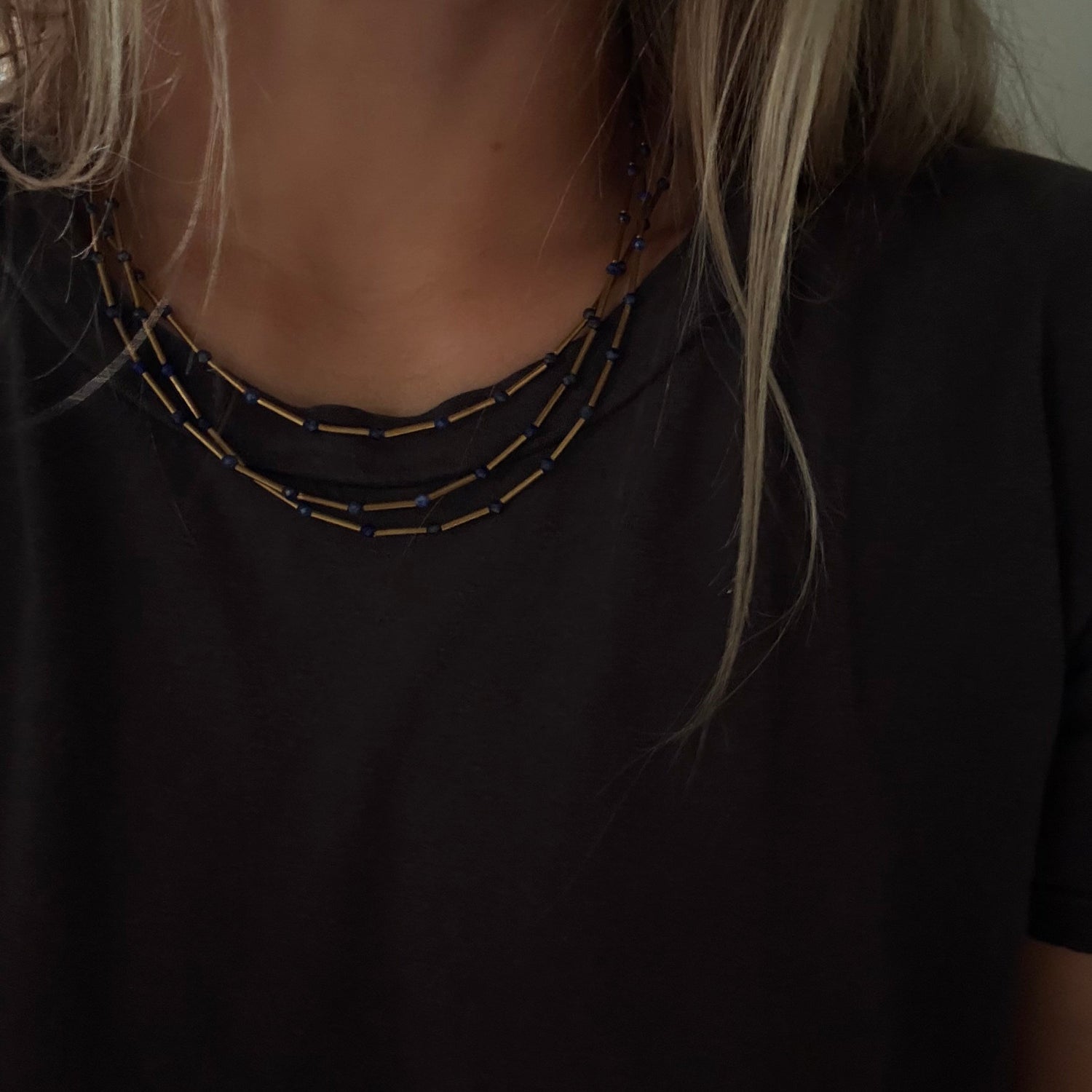 Close-up of a person wearing a layered necklace with small gold and dark beads over a black top.