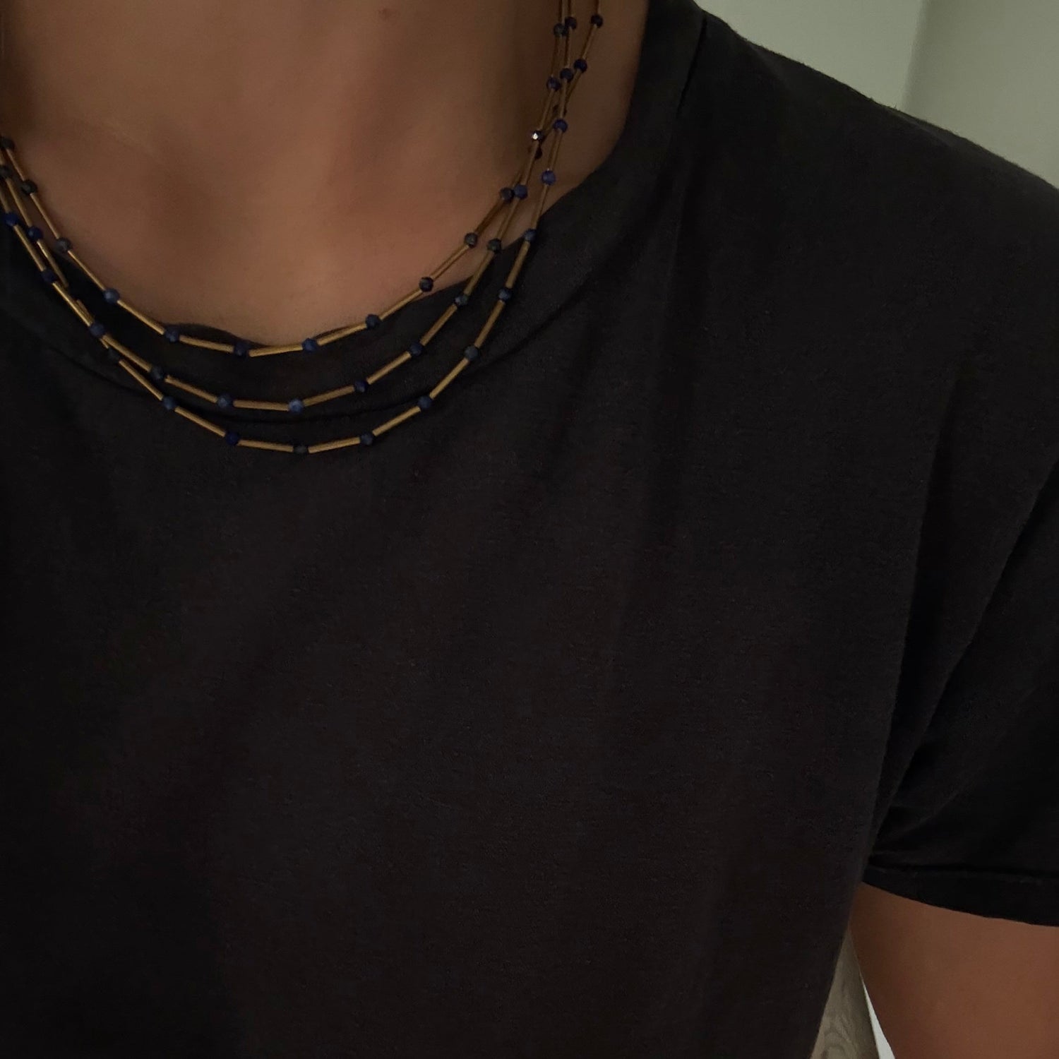 A close-up of a person wearing a black short-sleeve t-shirt and a multi-strand beaded necklace with black and gold beads.