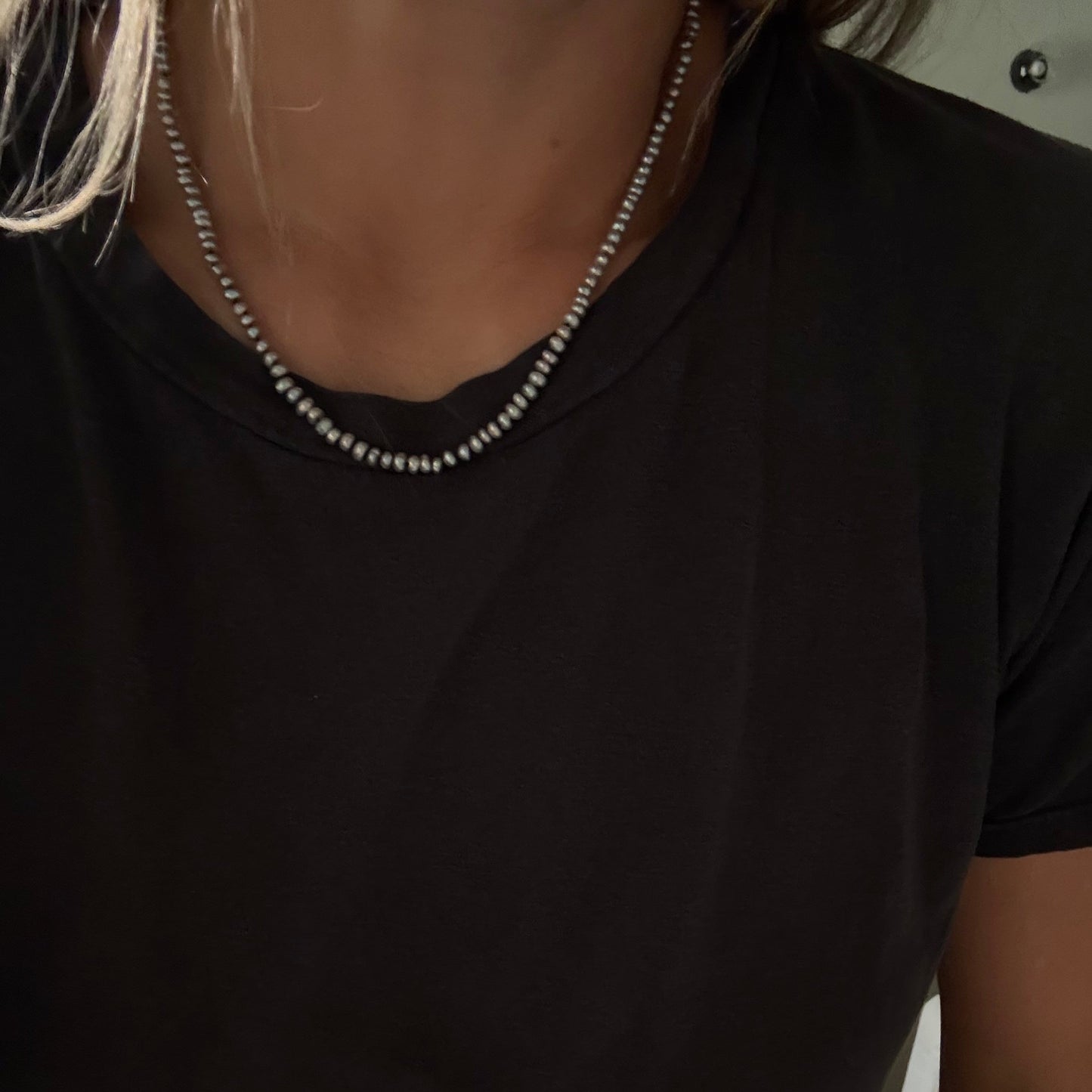 A close-up of a person wearing a gray freshwater pearl necklace  over a black t-shirt.