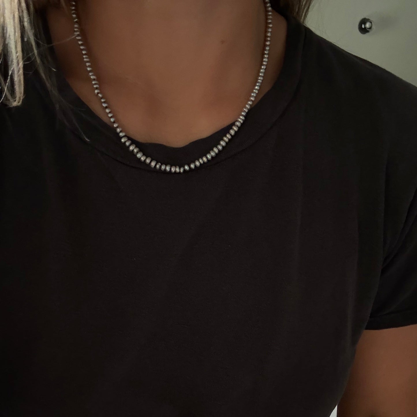 A close-up of a person wearing a gray freshwater pearl necklace  with a black t-shirt.
