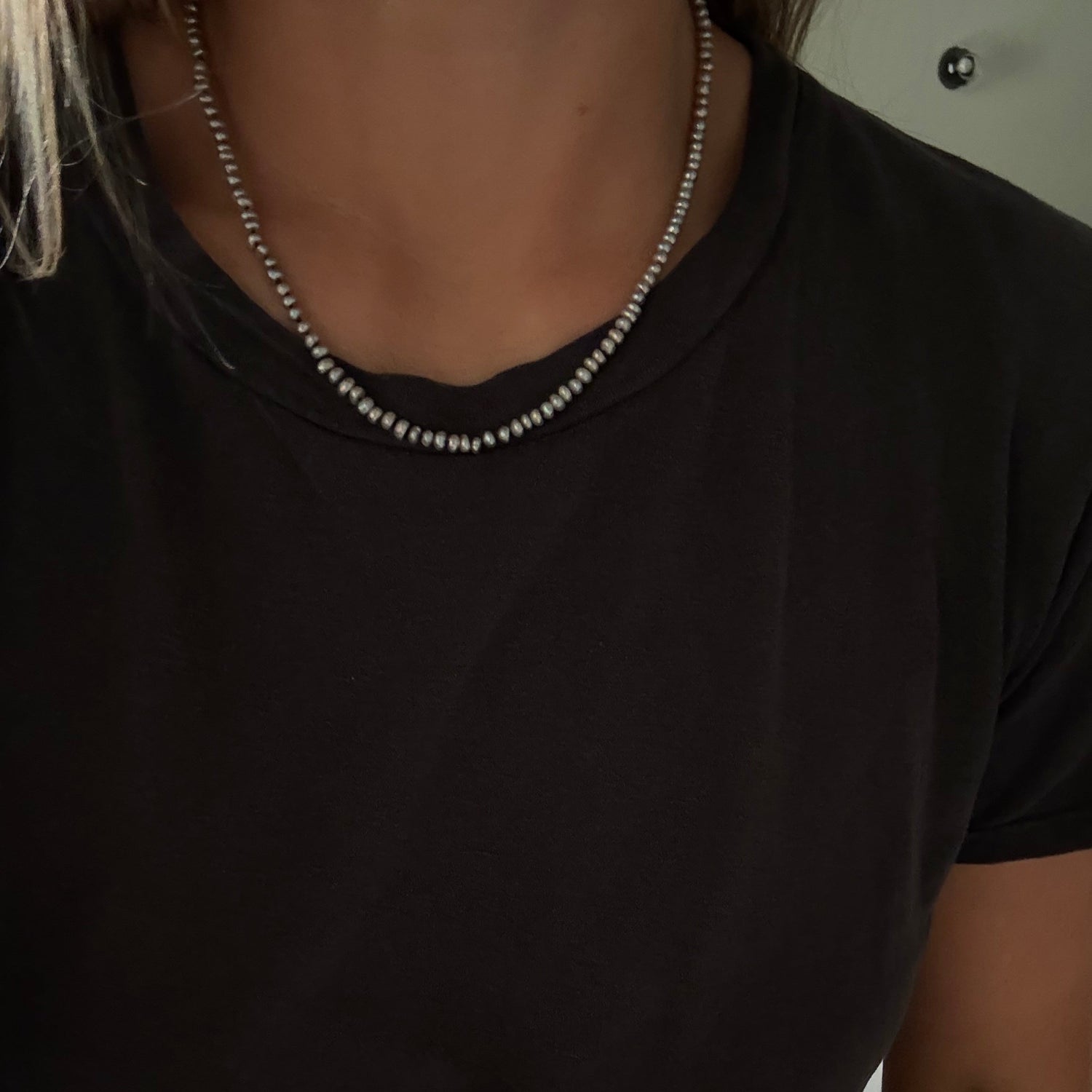 A close-up of a person wearing a gray freshwater pearl necklace  with a black t-shirt.