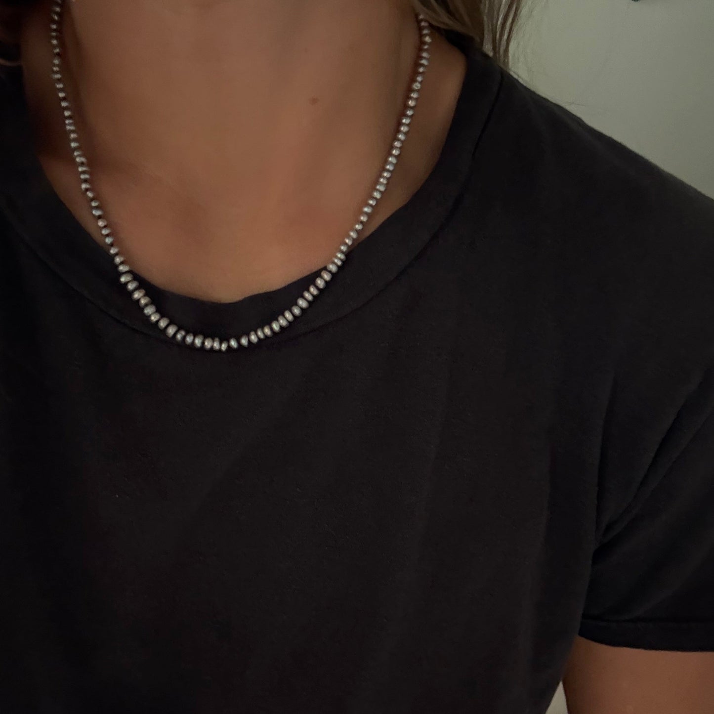 A close-up of a person wearing a gray freshwater pearl necklace  over a black t-shirt.