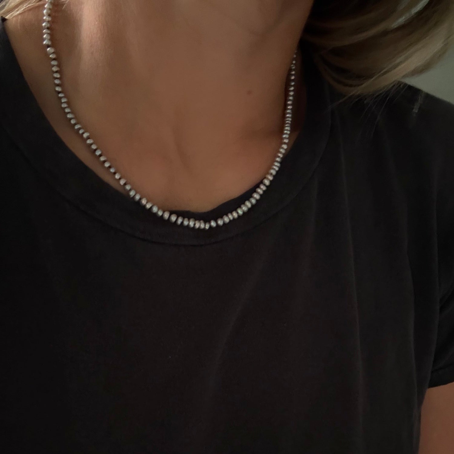 A close-up of a person wearing a delicate gray freshwater pearl necklace  with a small central charm, styled with a black t-shirt.