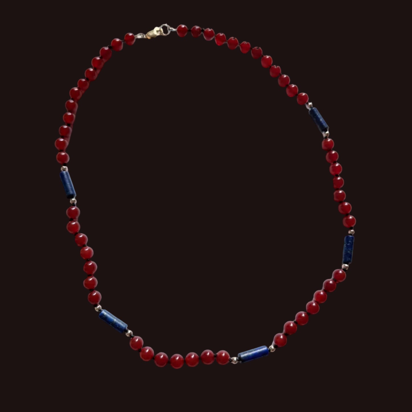 A beaded necklace featuring round red beads and alternating dark blue cylindrical spacer beads separated by small silver-toned metal links, displayed on a white surface.