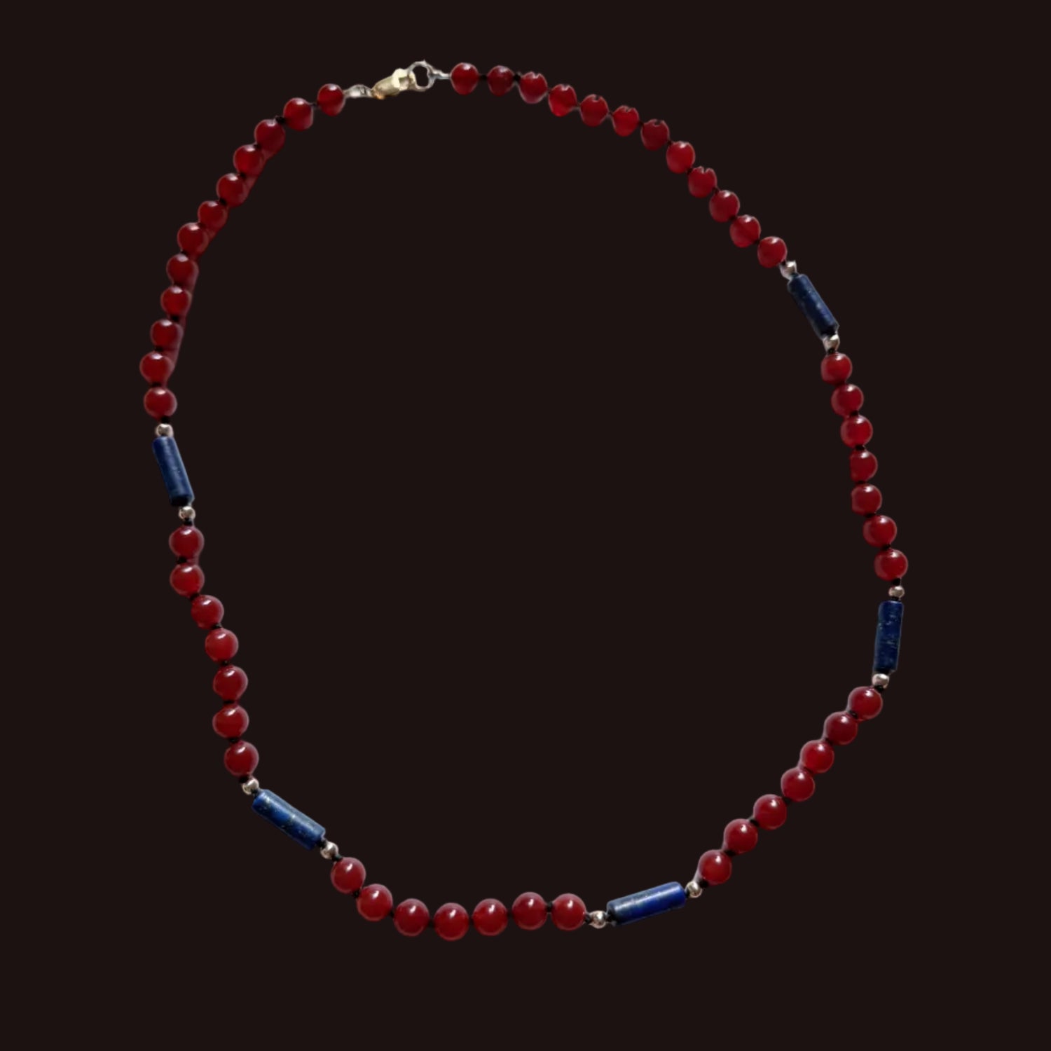 A beaded necklace featuring round red beads and alternating dark blue cylindrical spacer beads separated by small silver-toned metal links, displayed on a white surface.