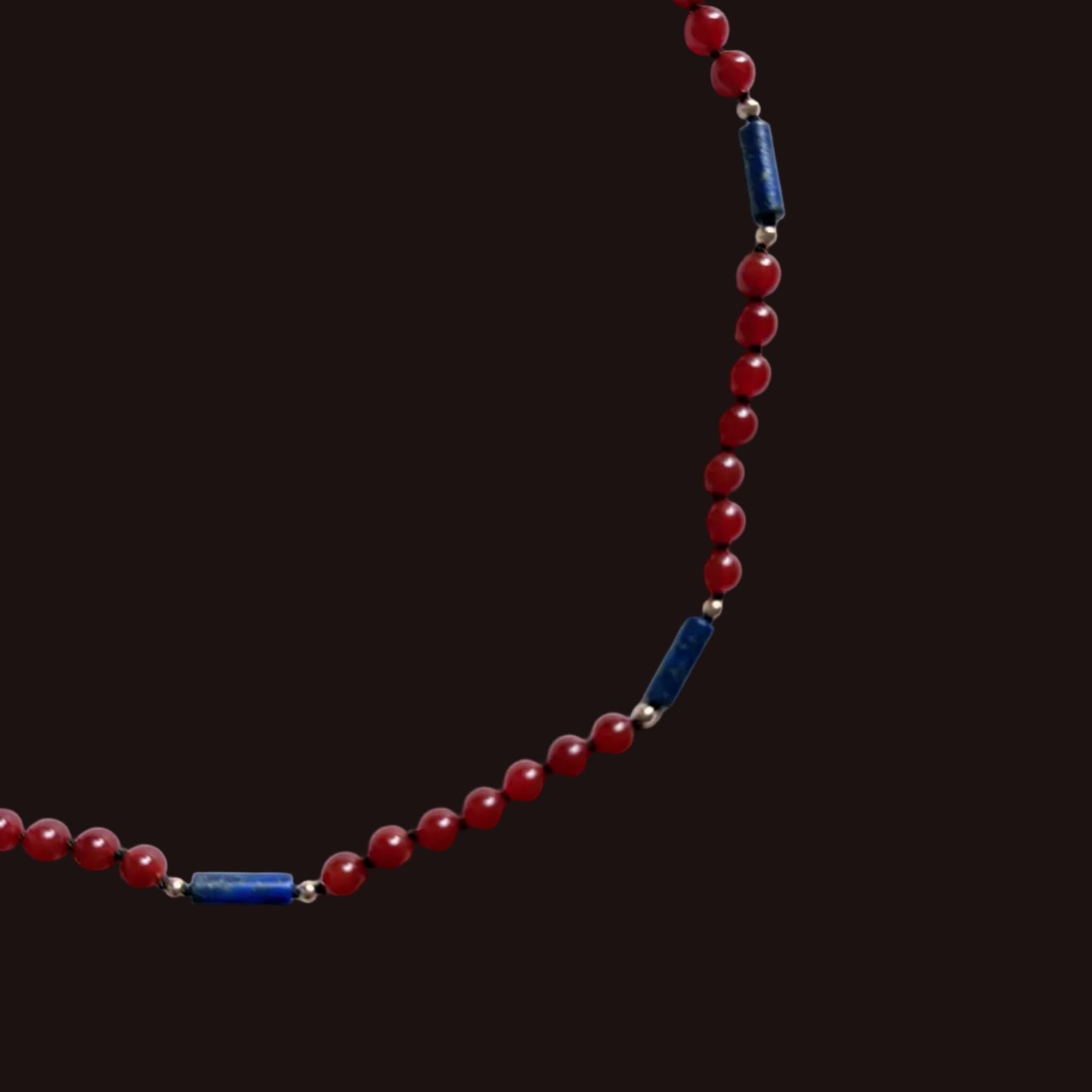 A beaded necklace featuring round red beads and several dark blue cylindrical spacer beads separated by small silver-toned metal rings, displayed on a plain light gray background.