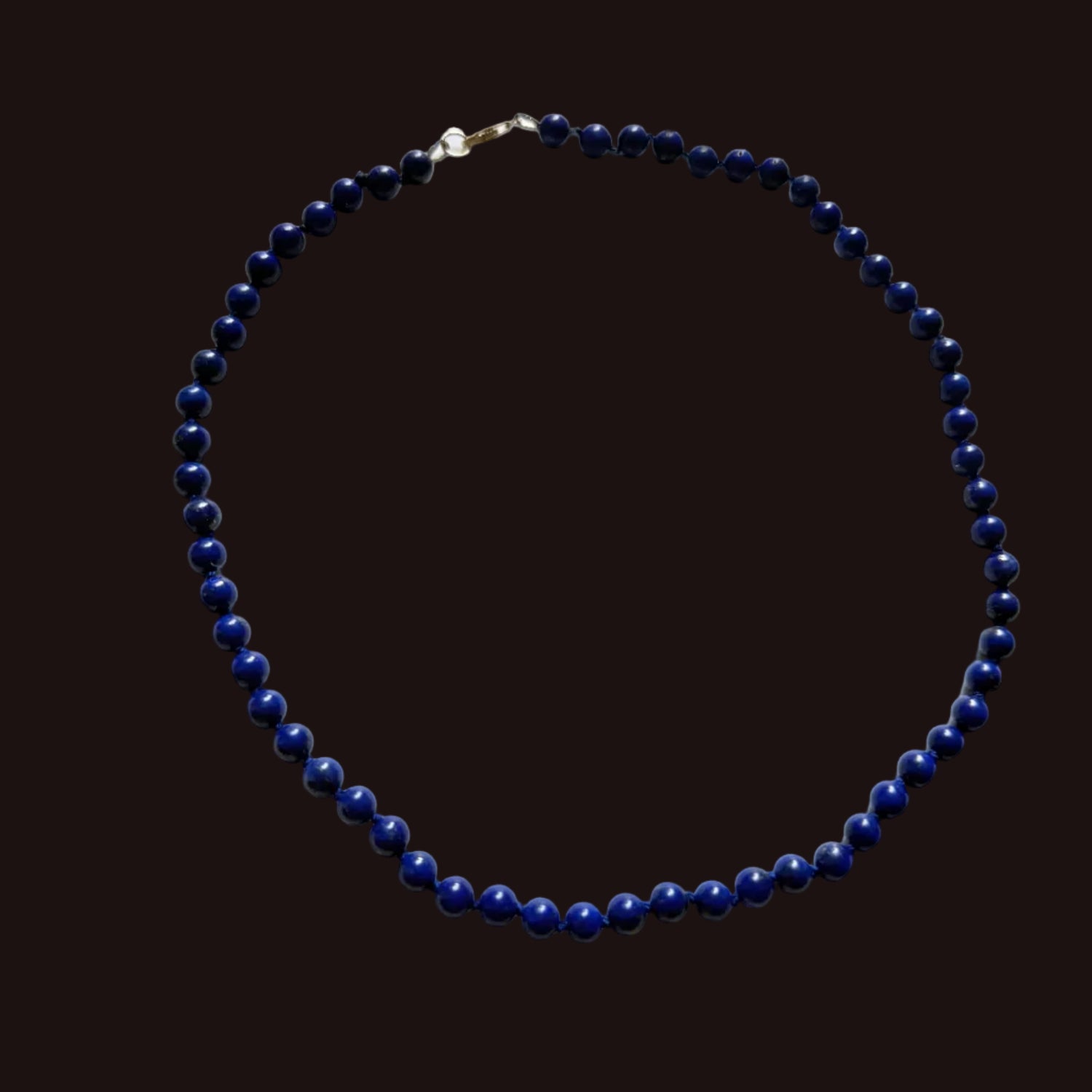 A beaded necklace made of small dark blue lapis lazuli-style beads with a gold clasp, laid flat on a white surface.