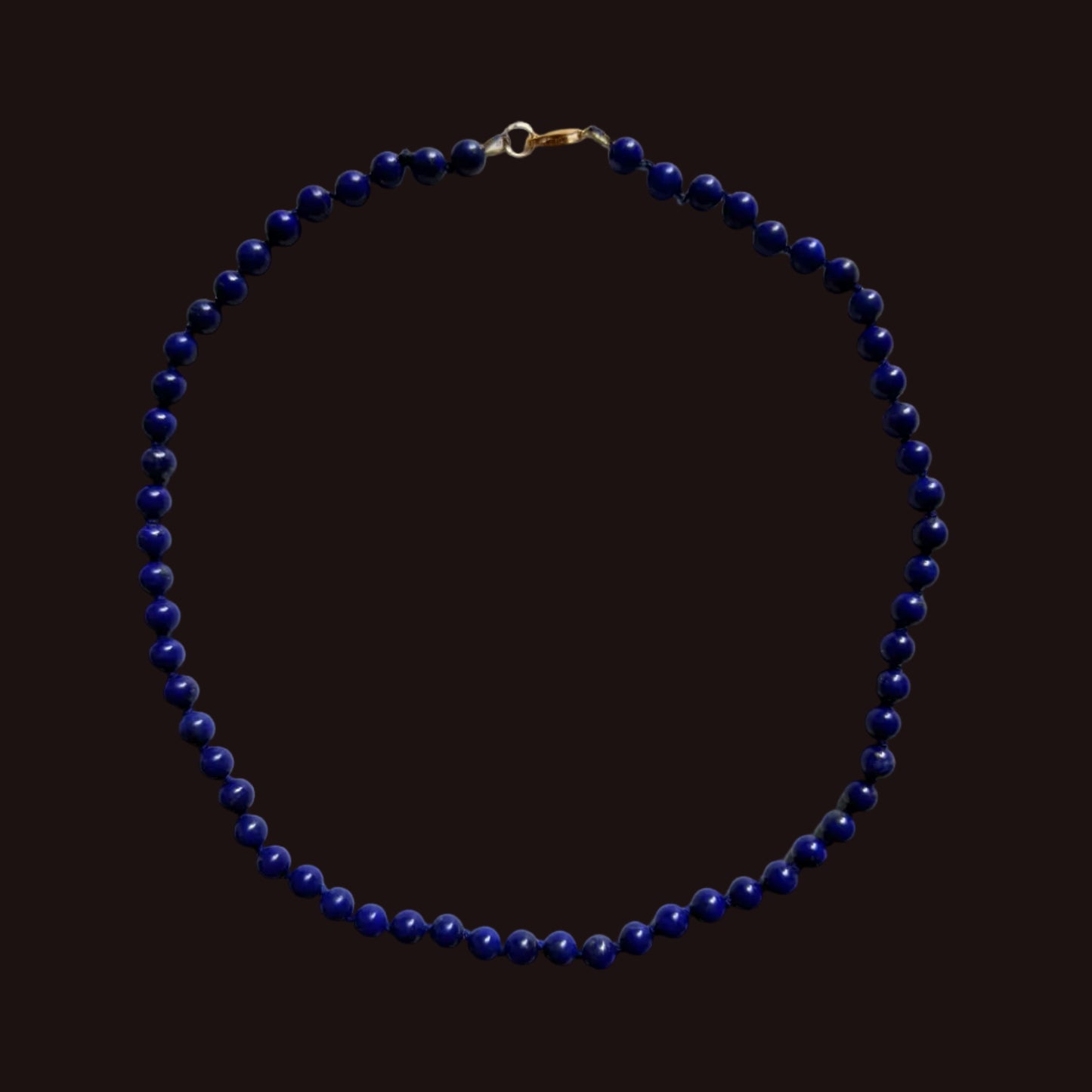 A beaded necklace made of small dark blue beads with a gold clasp, laid flat on a light gray background.