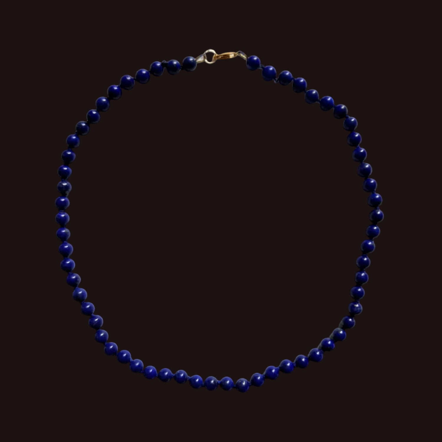 A beaded necklace made of small dark blue beads with a gold clasp, laid flat on a light gray background.