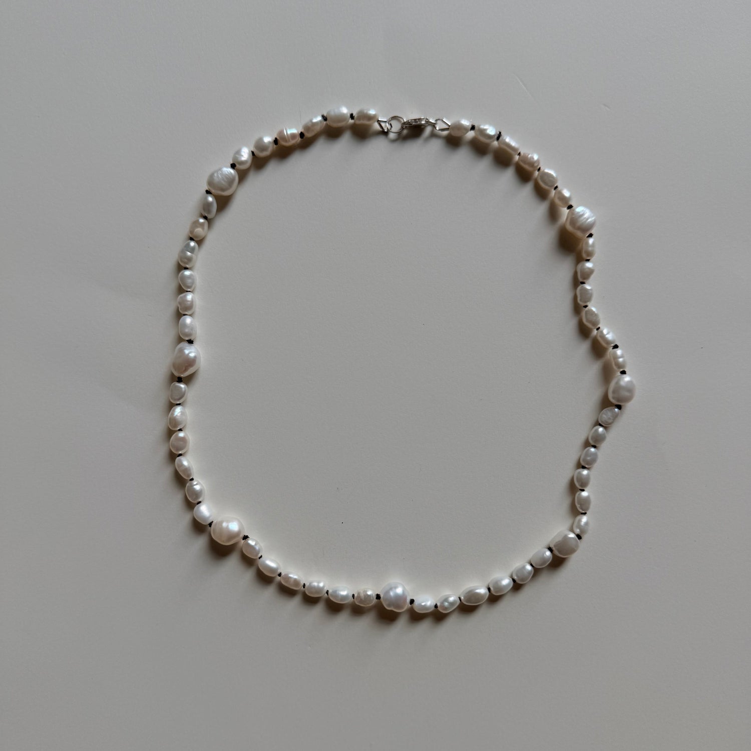 A strand necklace made of irregular white freshwater pearls with a small silver clasp, laid flat on a light gray surface.