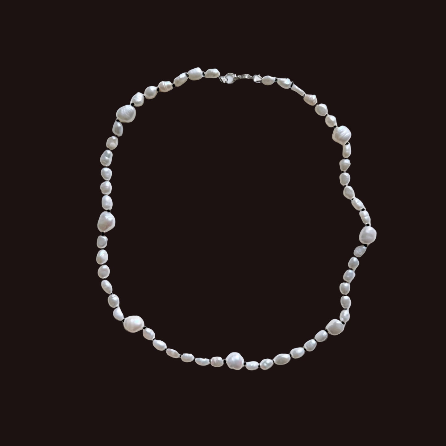 A beaded necklace made of irregular white pearls and small silver spacer beads, arranged in a loose circle on a plain light gray background.