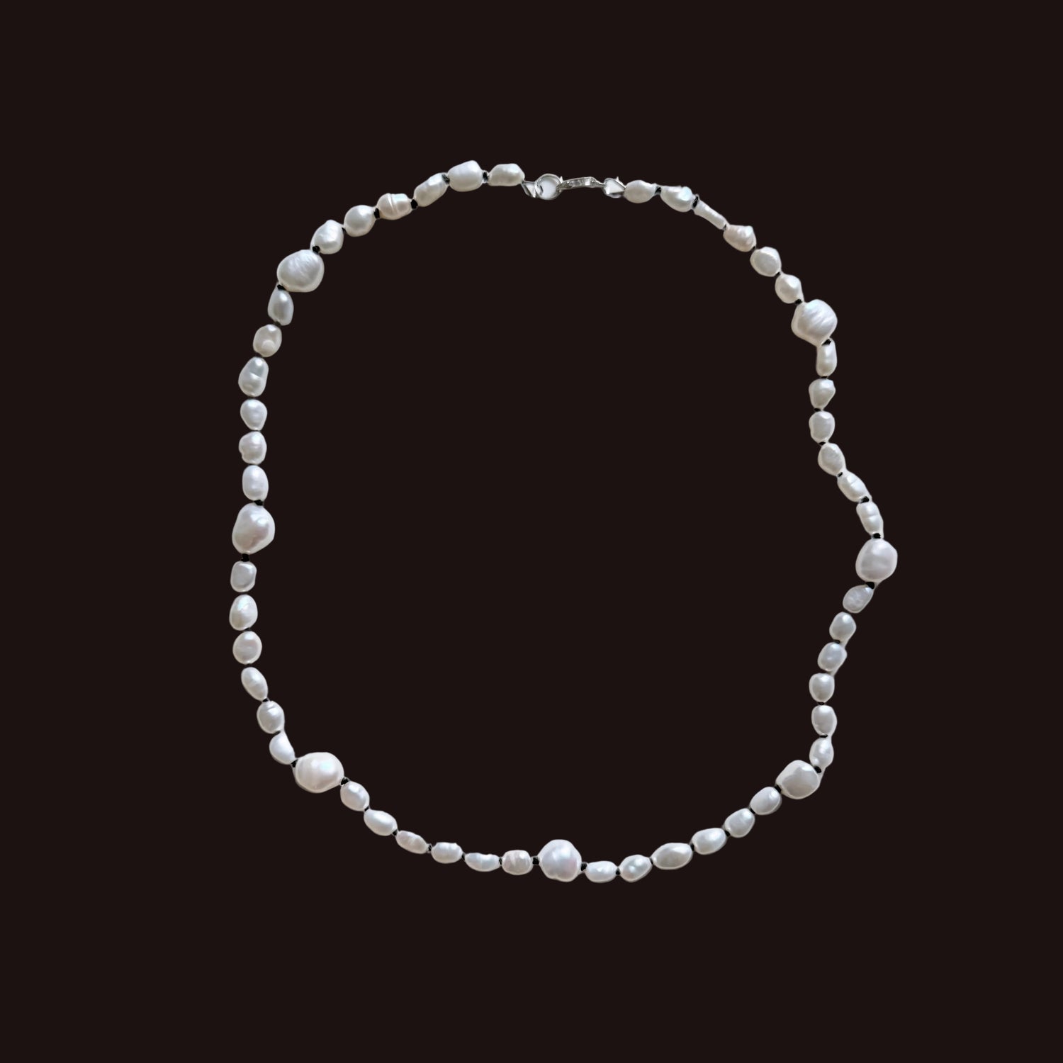 A beaded necklace made of irregular white pearls and small silver spacer beads, arranged in a loose circle on a plain light gray background.