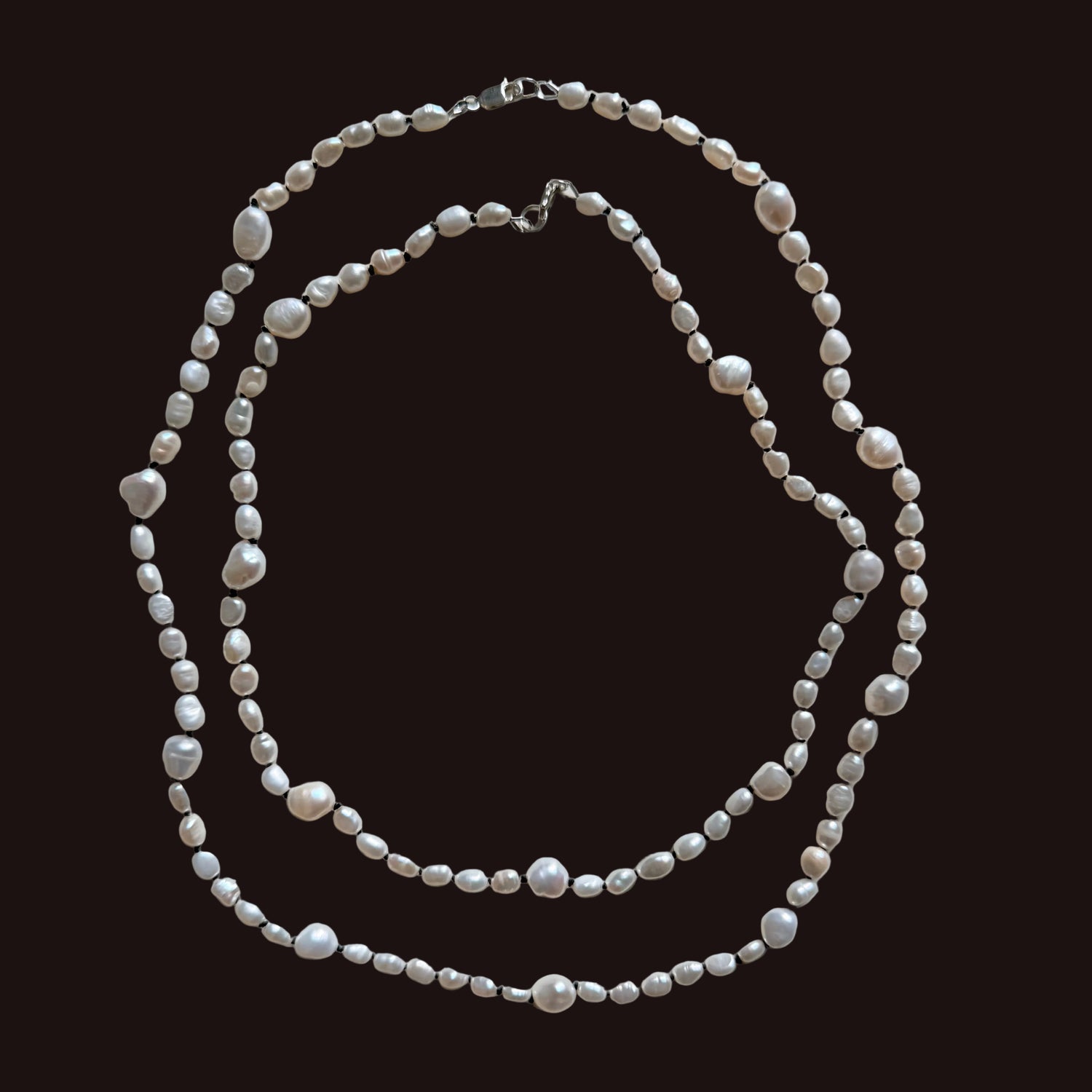A double-strand necklace made of irregular white freshwater pearls and small silver-toned beads, laid flat on a light gray background. A measurement label is visible along the bottom edge of the photo.