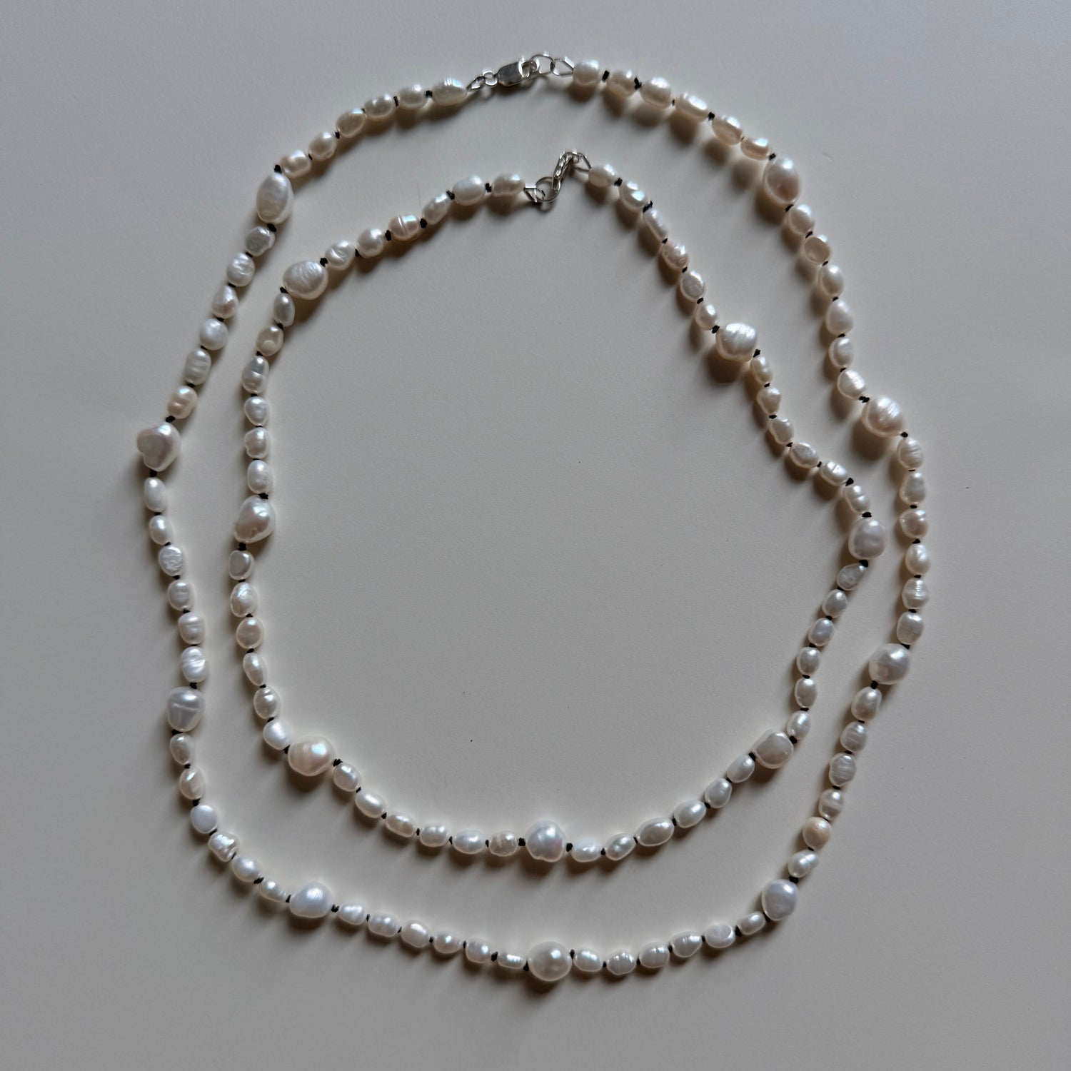 A double-strand pearl necklace with irregular white pearls and silver-tone clasps, laid flat on a light gray background.