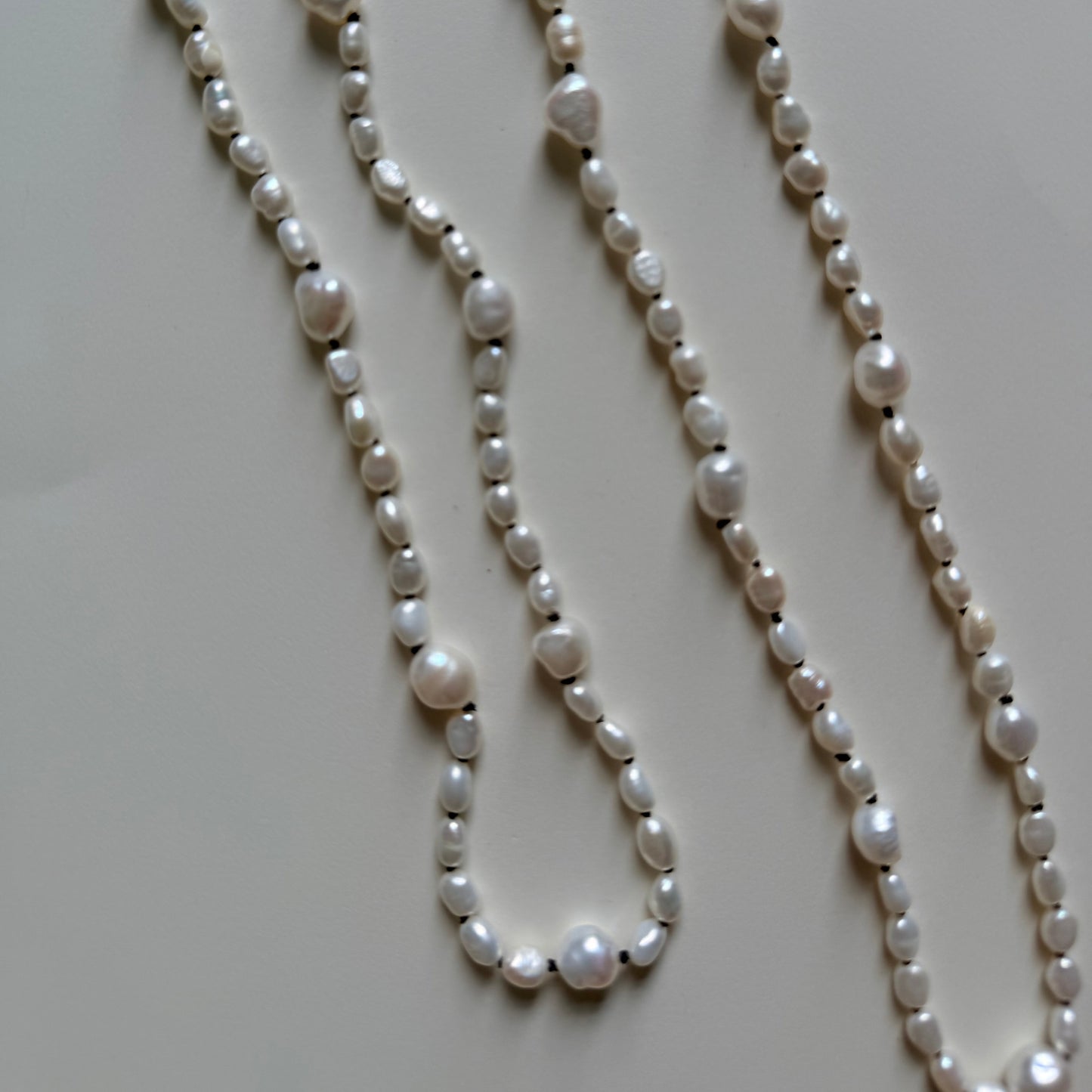 A long baroque pearl necklace with irregular white pearls and small silver spacer beads, laid out on a light beige surface.