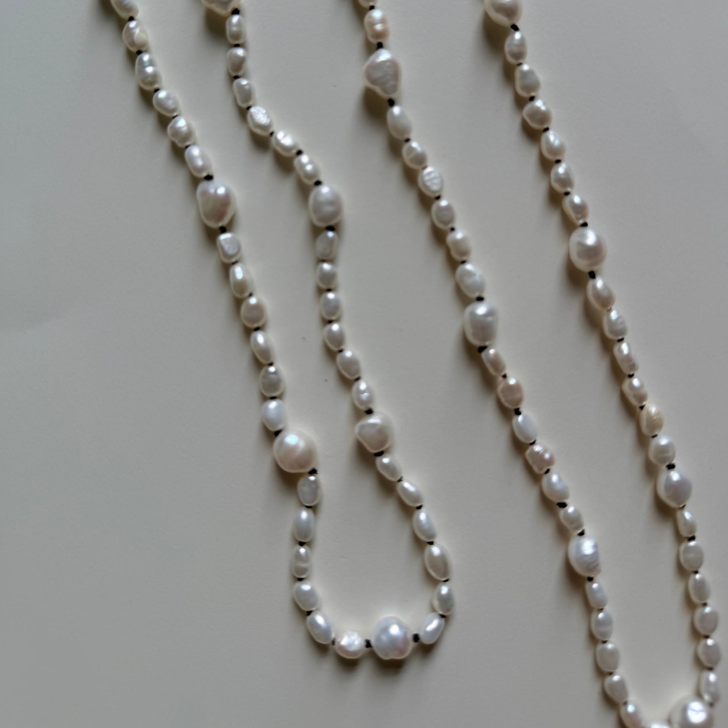 A long baroque pearl necklace with irregular white pearls and small silver spacer beads, laid out on a light beige surface.