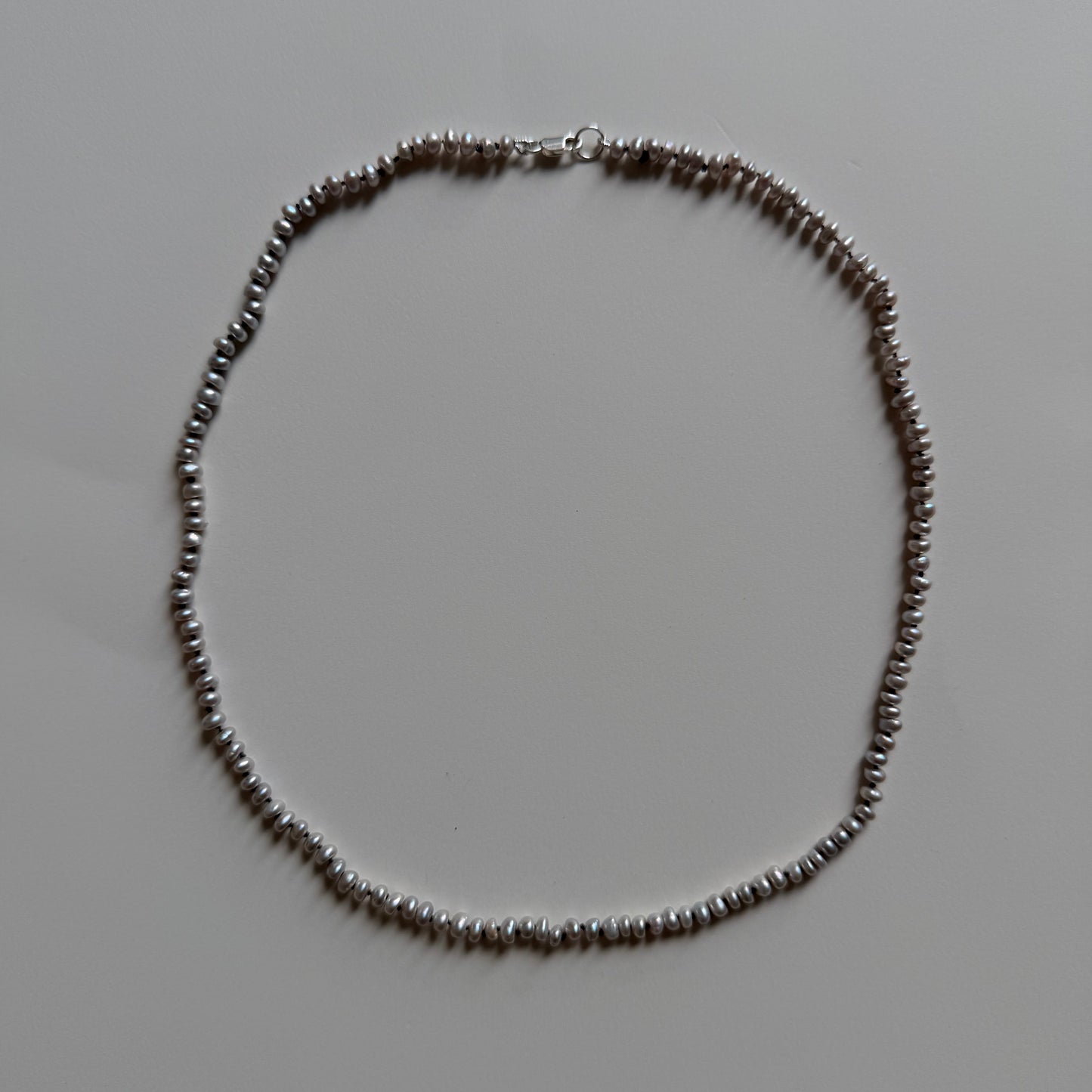 A delicate gray frshwater pearl necklace arranged in a circle on a plain light gray background.
