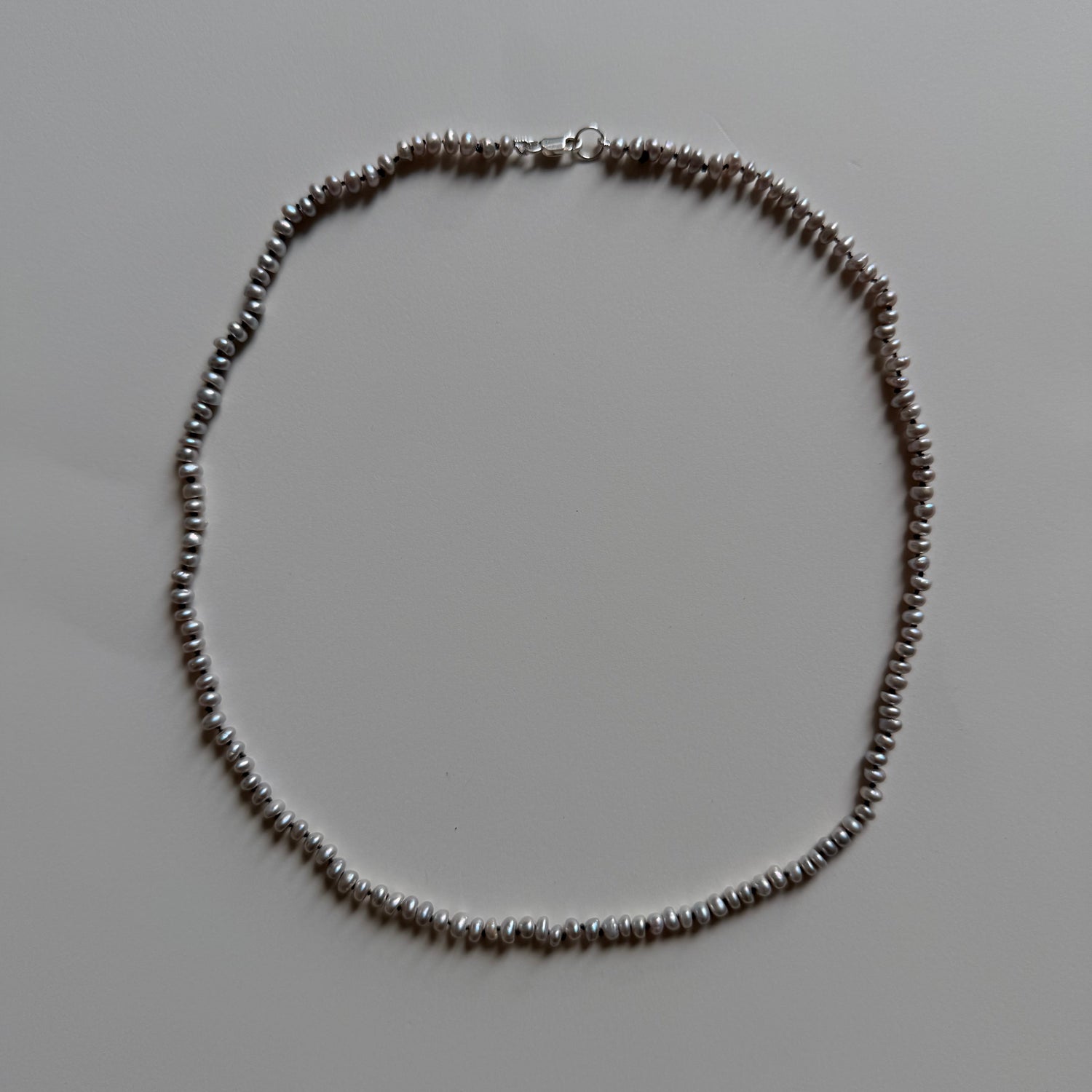 A delicate gray frshwater pearl necklace arranged in a circle on a plain light gray background.