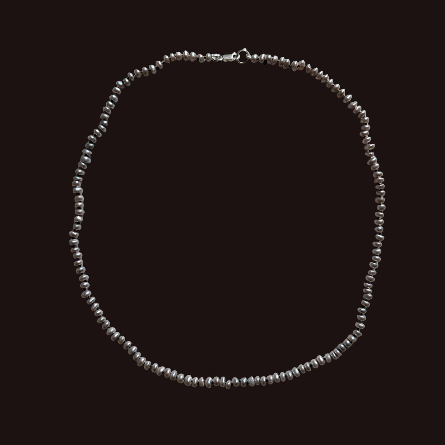 A delicate gray freshwater  pearl necklace and a lobster clasp, laid flat on a light gray background.