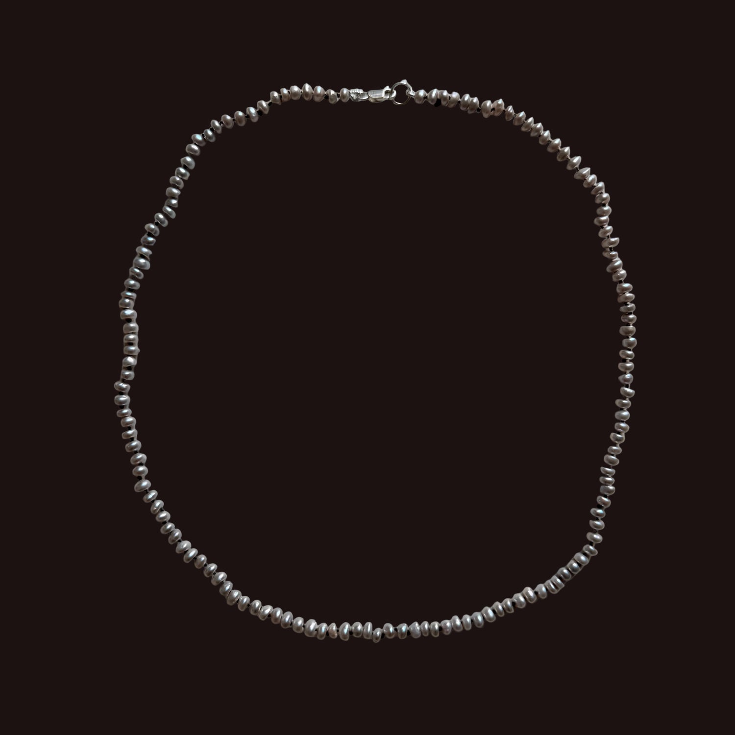 A delicate gray freshwater  pearl necklace and a lobster clasp, laid flat on a light gray background.