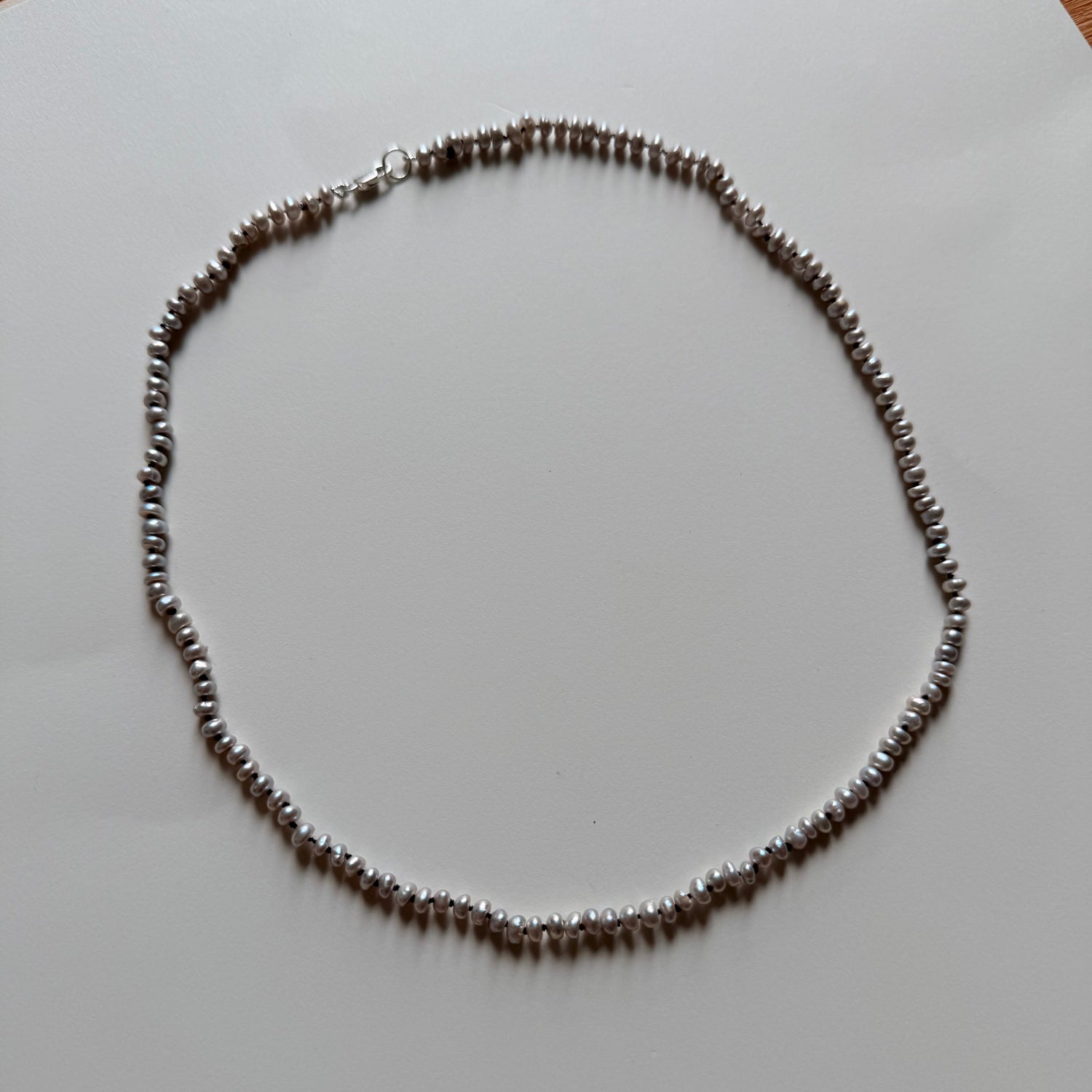 A gray freshwater pearl necklace, arranged in a circle on a plain white surface.