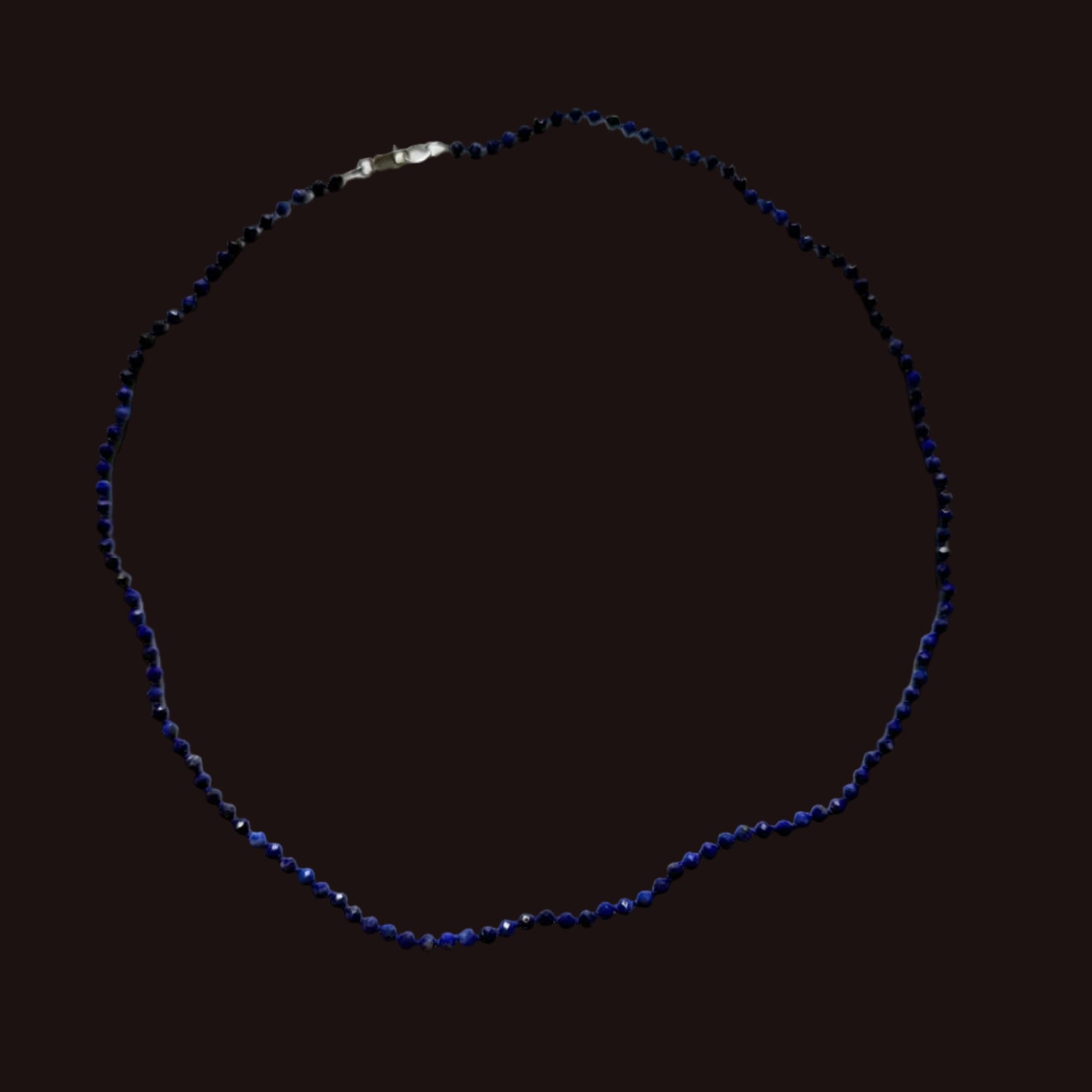 A beaded necklace made of small dark blue faceted beads with a silver clasp, laid out in a circle on a white sheet of paper.