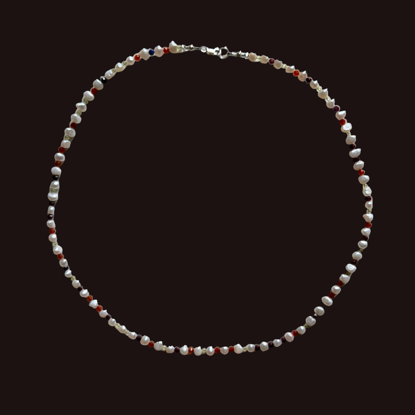 A beaded necklace made of small white, red, and dark brown beads with a silver clasp, laid flat on a light gray background.