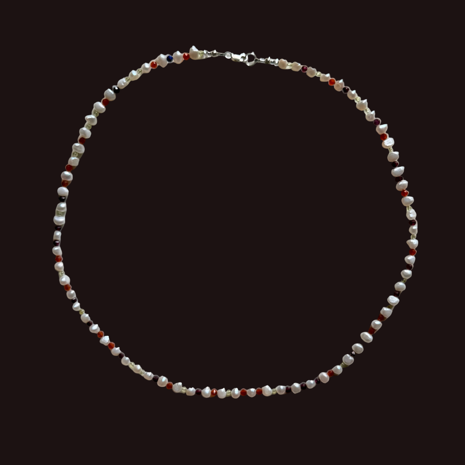 A beaded necklace made of small white, red, and dark brown beads with a silver clasp, laid flat on a light gray background.