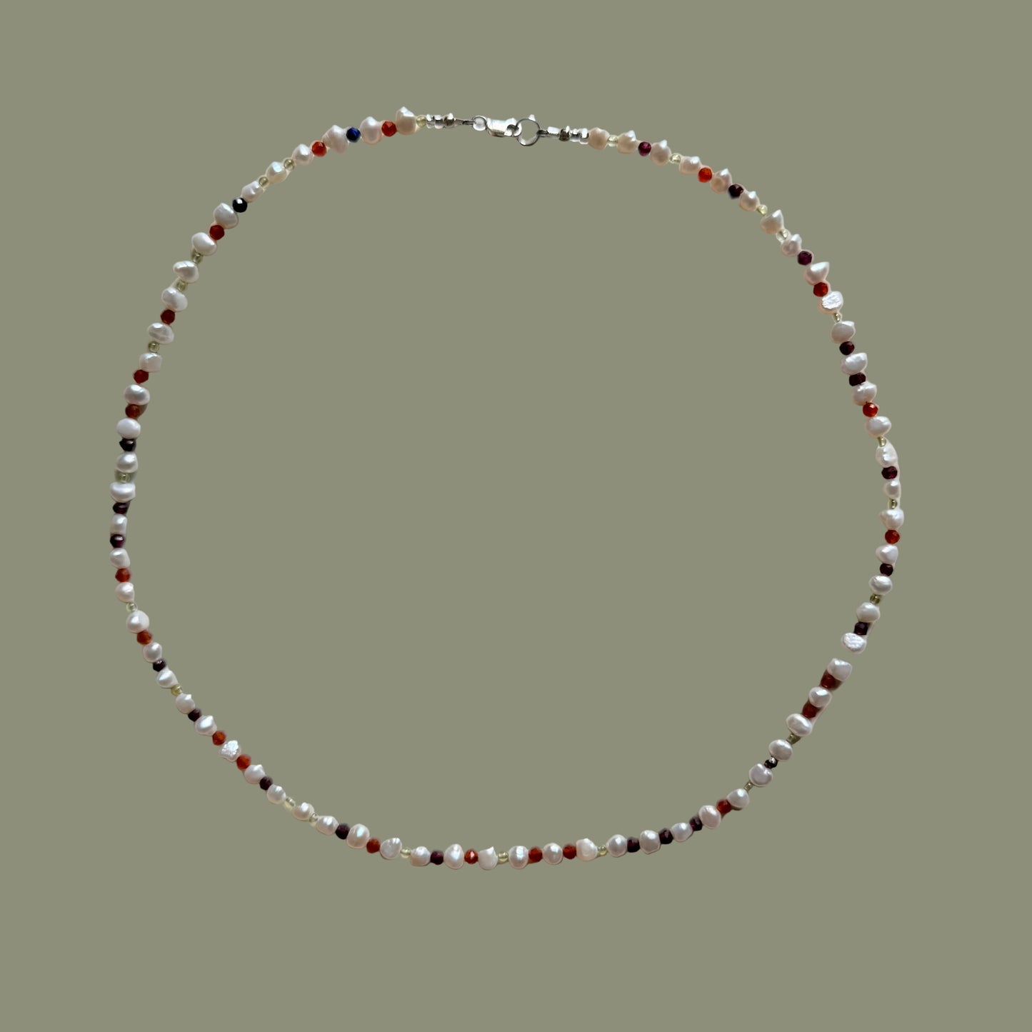 A beaded necklace arranged in a circle on a plain light background. The necklace features small faceted beads in white, translucent clear, dark gray, and red, with a silver clasp visible at the top.