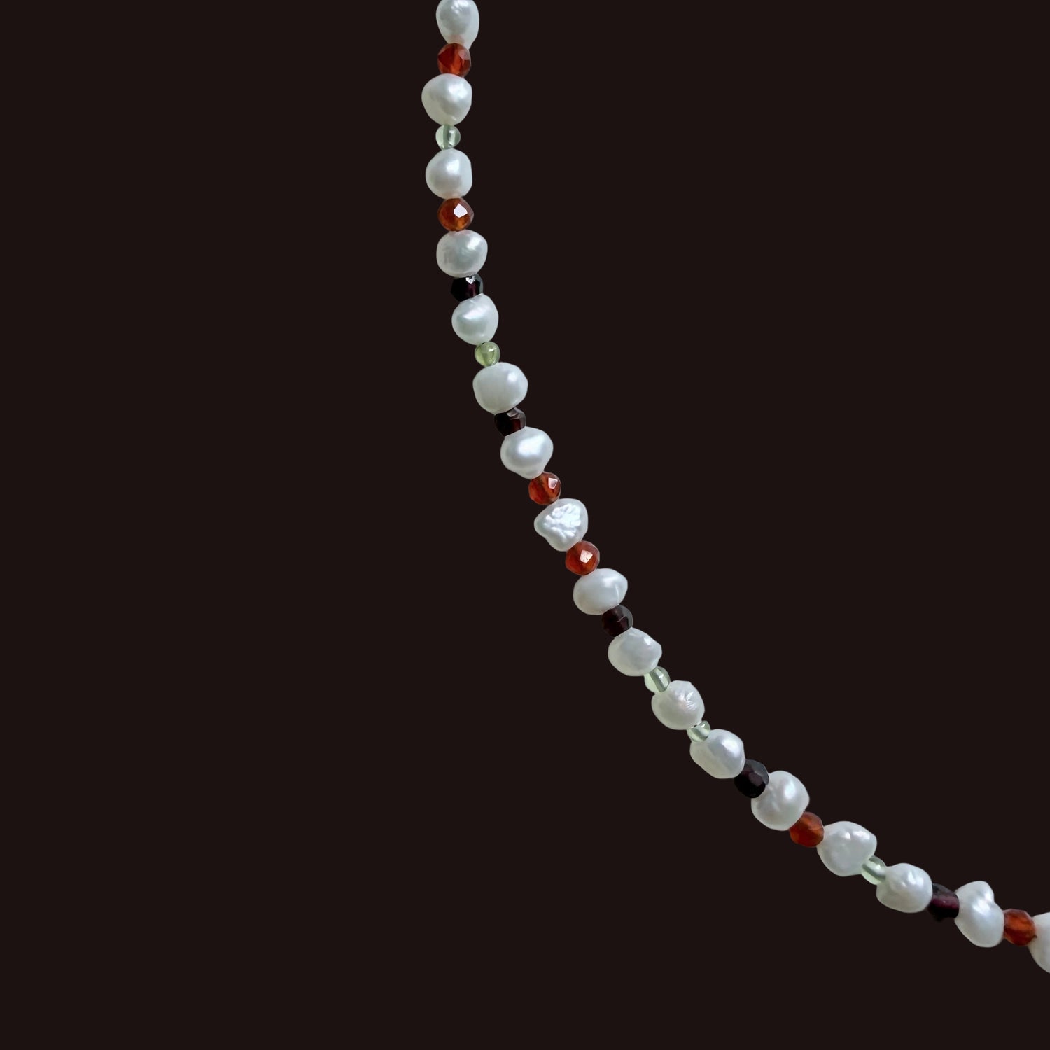 A beaded strand necklace featuring white baroque pearls and small faceted beads in red, dark brown, and light green, arranged diagonally on a light gray background.