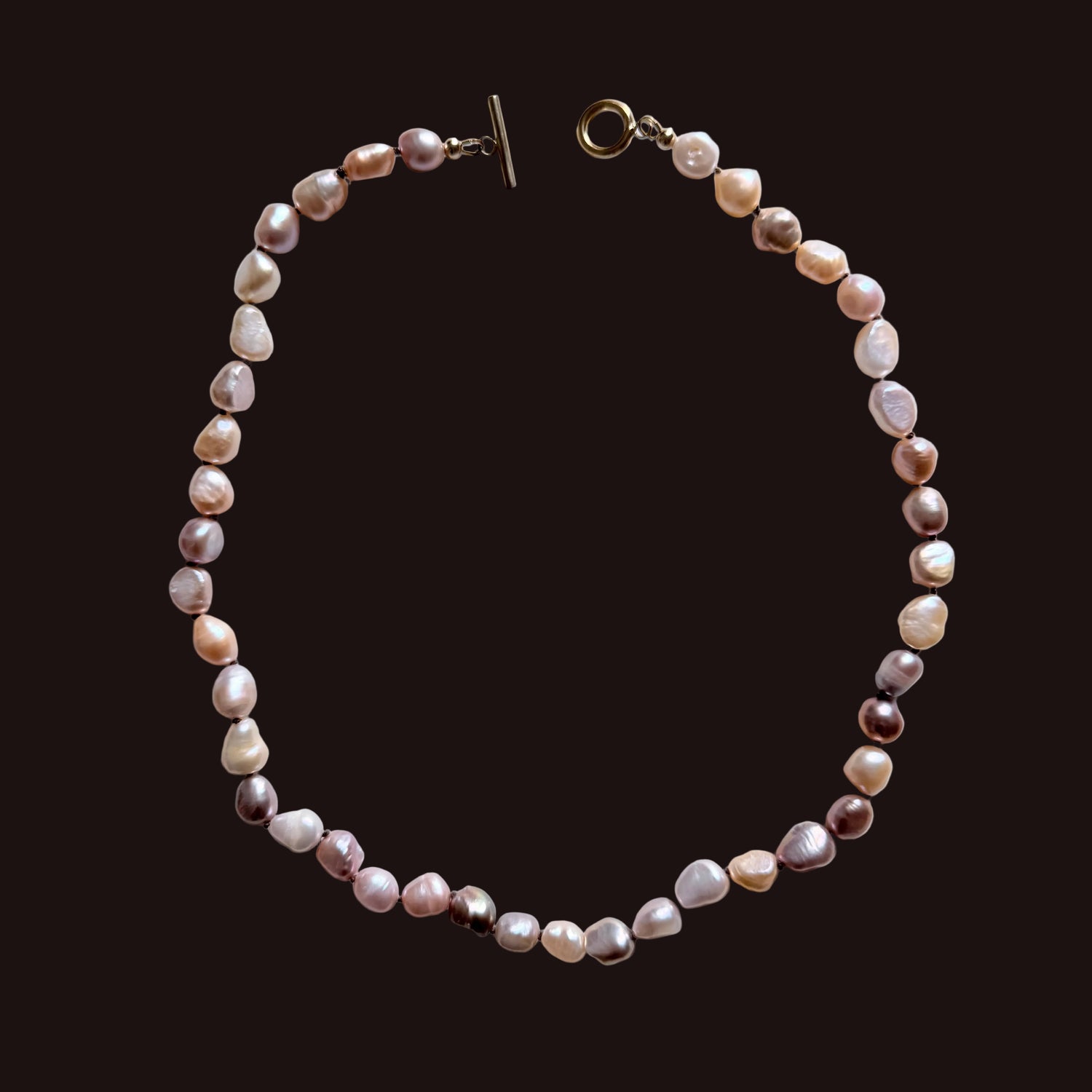 A beaded necklace made of irregular, baroque-style pearls in soft pink, peach, cream, and mauve tones, arranged in a circle on a light gray background. It features a gold-tone toggle clasp on one end and a lobster clasp on the other.